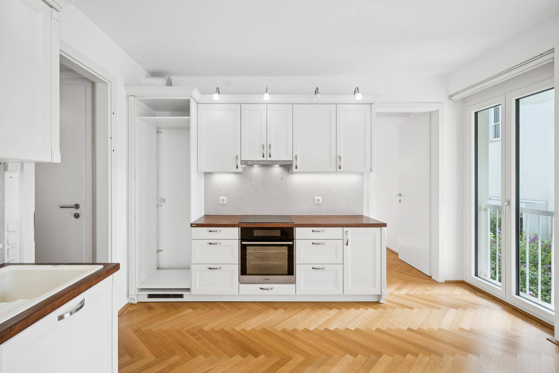 Moderne Einbauküche mit weißen Schränken, Holzarbeitsplatte und integriertem Backofen.