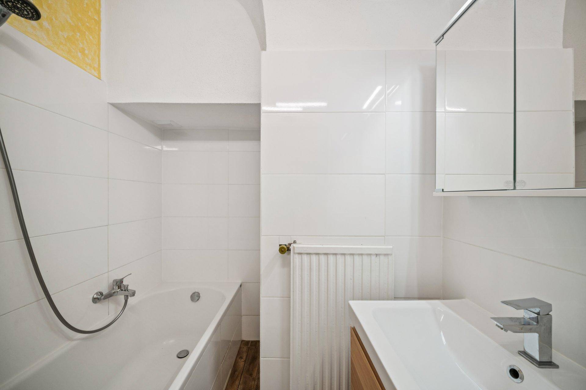 Modernes Badezimmer mit weißen Fliesen, Badewanne, Waschbecken und beheiztem Handtuchhalter.