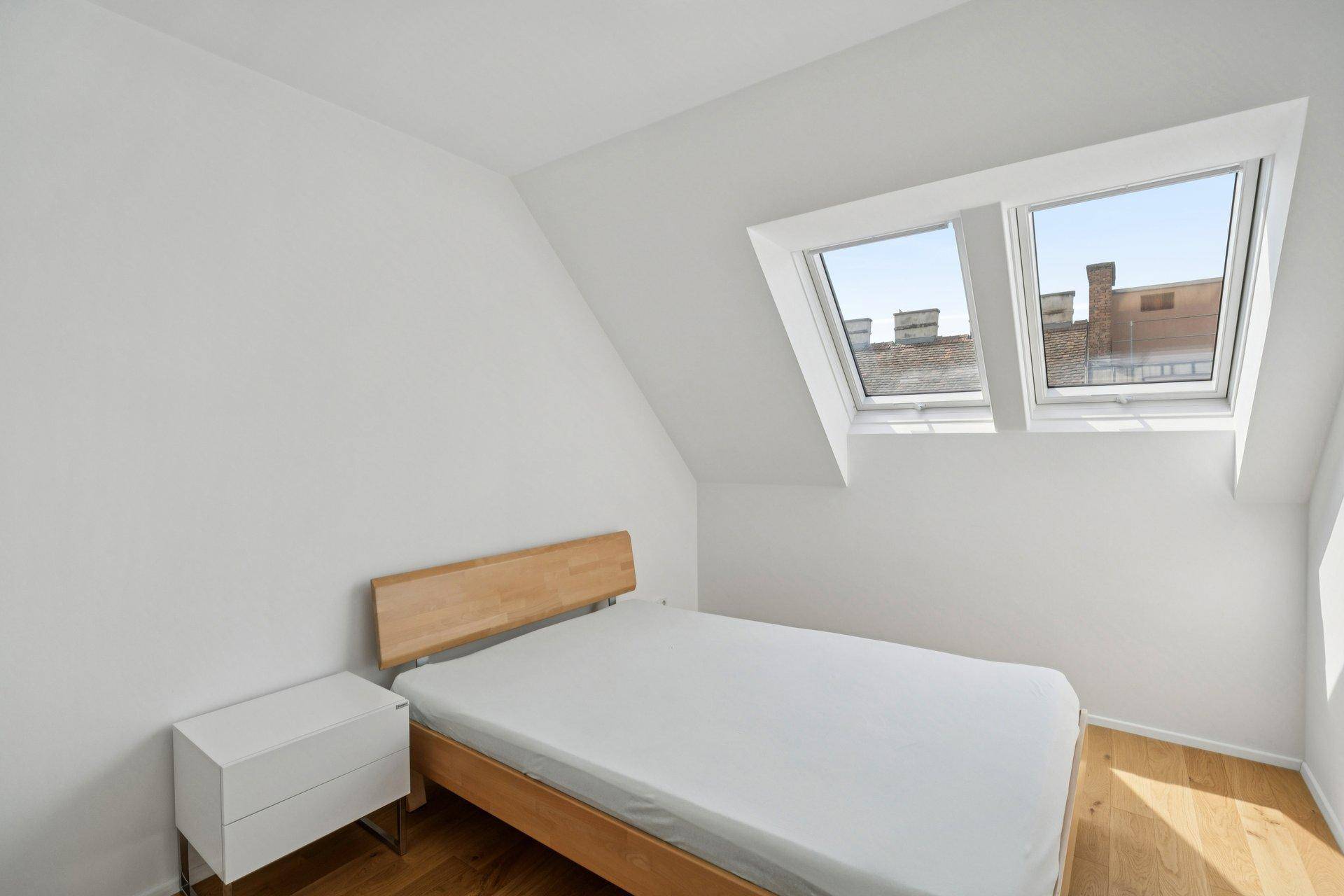 Helles Schlafzimmer im Dachgeschoss mit Holzbett, Dachfenstern und schrägen Wänden.