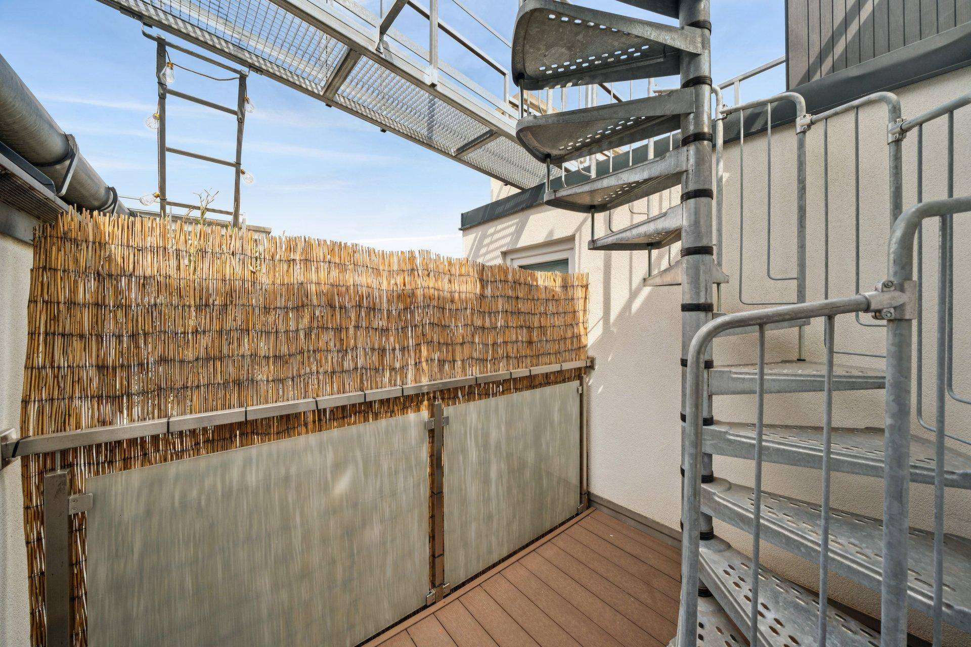 Kleiner Balkon mit Holzverkleidung und Metallwendeltreppe, die zur Dachterrasse führt.