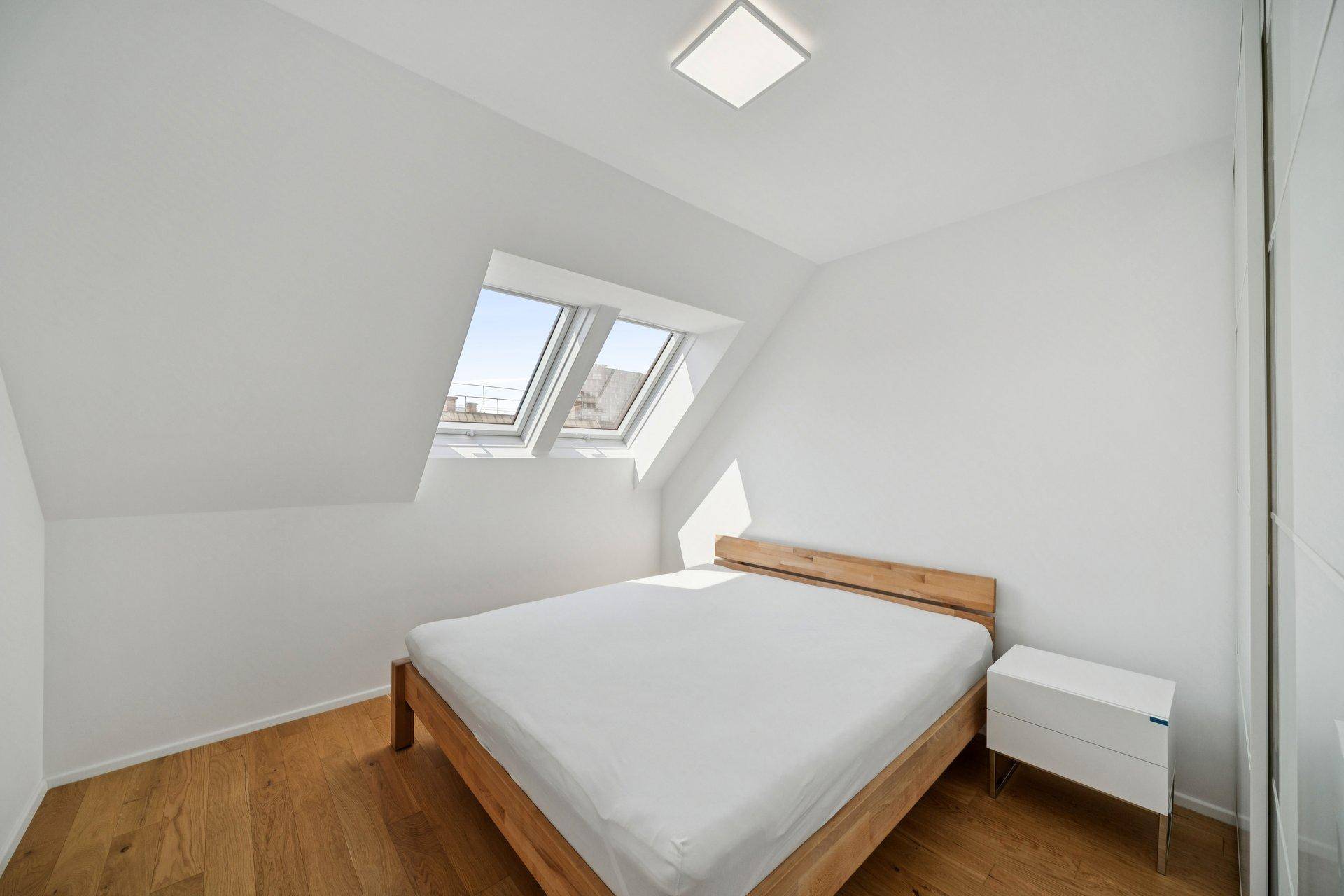 Gemütliches Schlafzimmer mit Holzboden, Dachfenstern und minimalistischer Einrichtung.