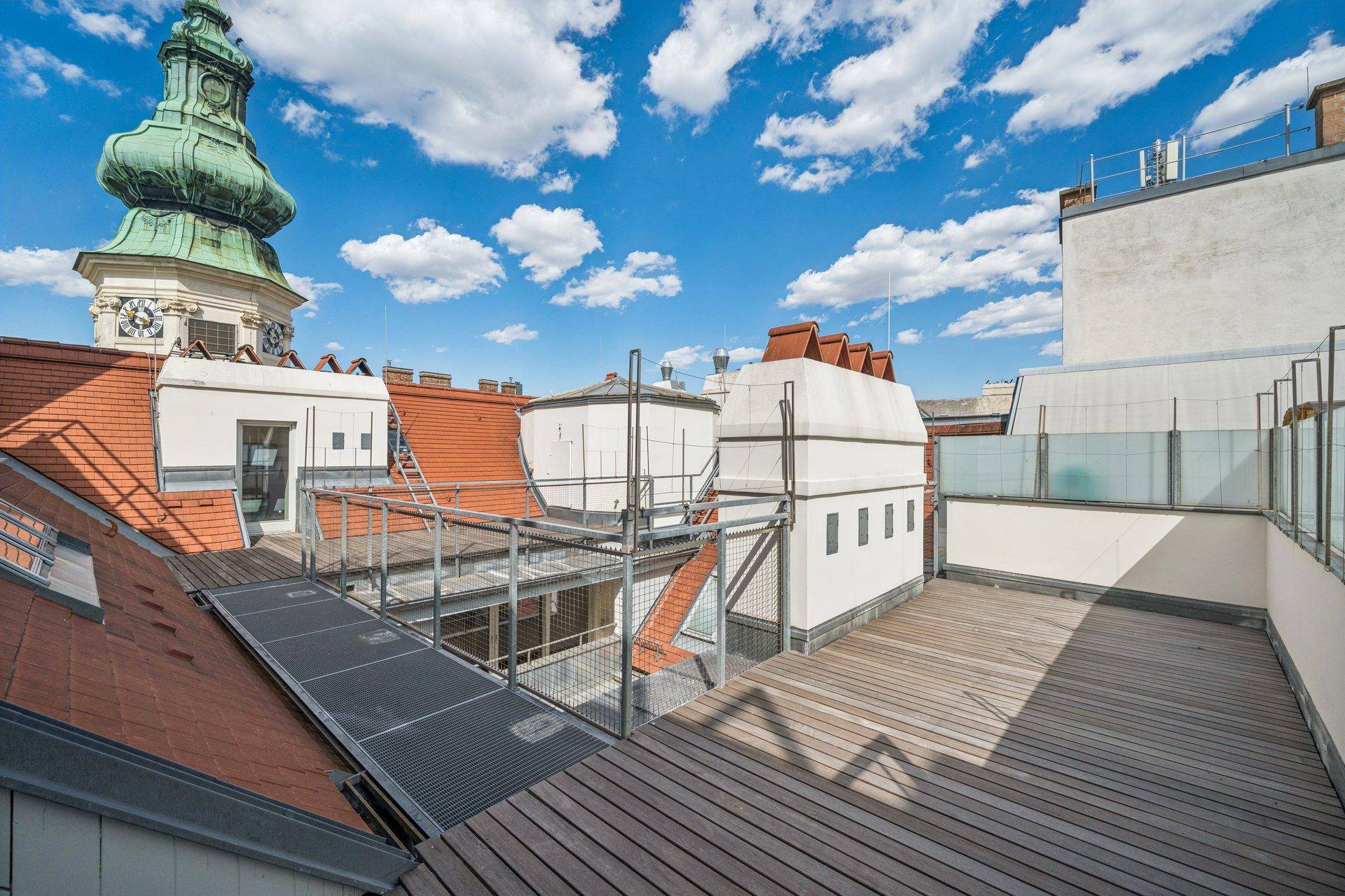 Geräumige Dachterrasse mit Holzboden und weitem Blick über die Dächer der Stadt und einen Kirchturm.