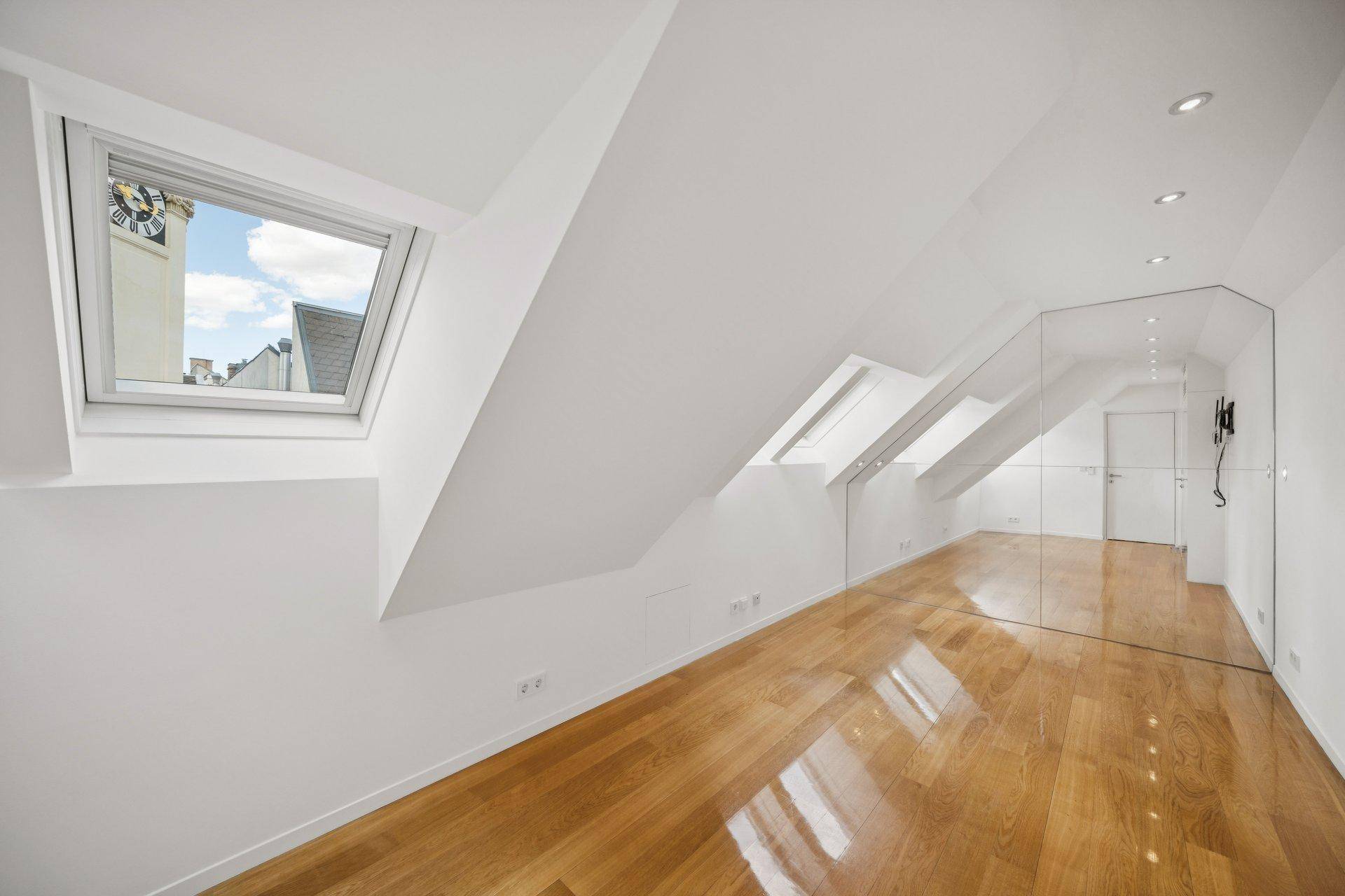 Heller Raum mit Holzfußboden, Dachfenstern und einer Spiegelfläche, ideal als Schlaf- oder Arbeitszimmer.