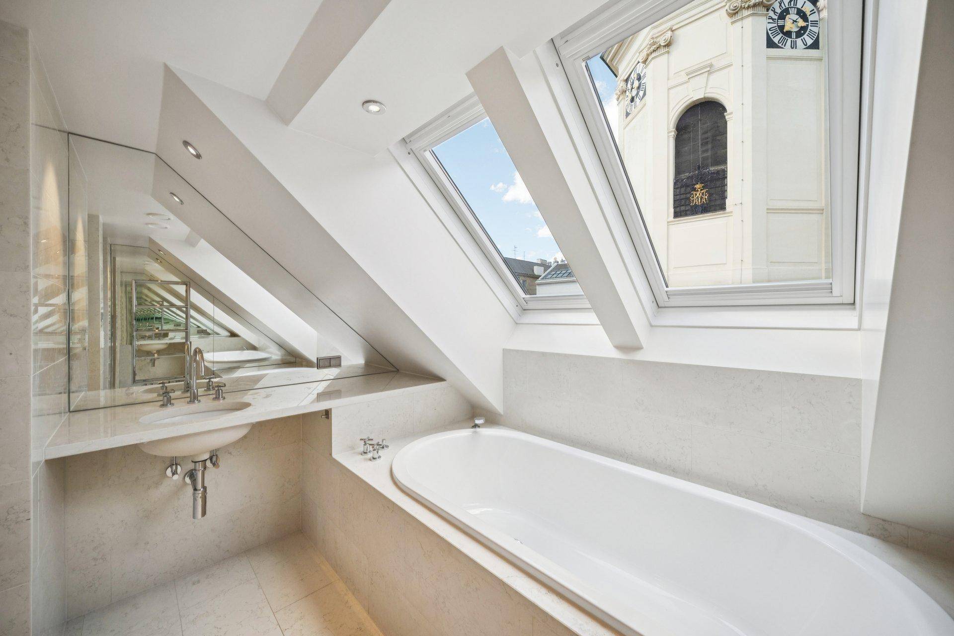 Modernes Badezimmer mit Badewanne, Einzelwaschbecken und Dachfenster mit Blick auf einen Kirchturm.