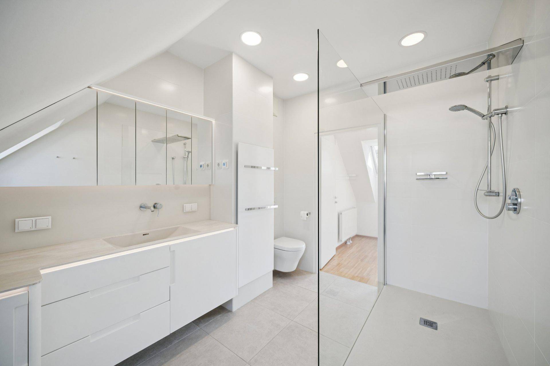 Modernes, helles Badezimmer mit begehbarer Dusche, Doppelwaschbecken und Dachschräge.