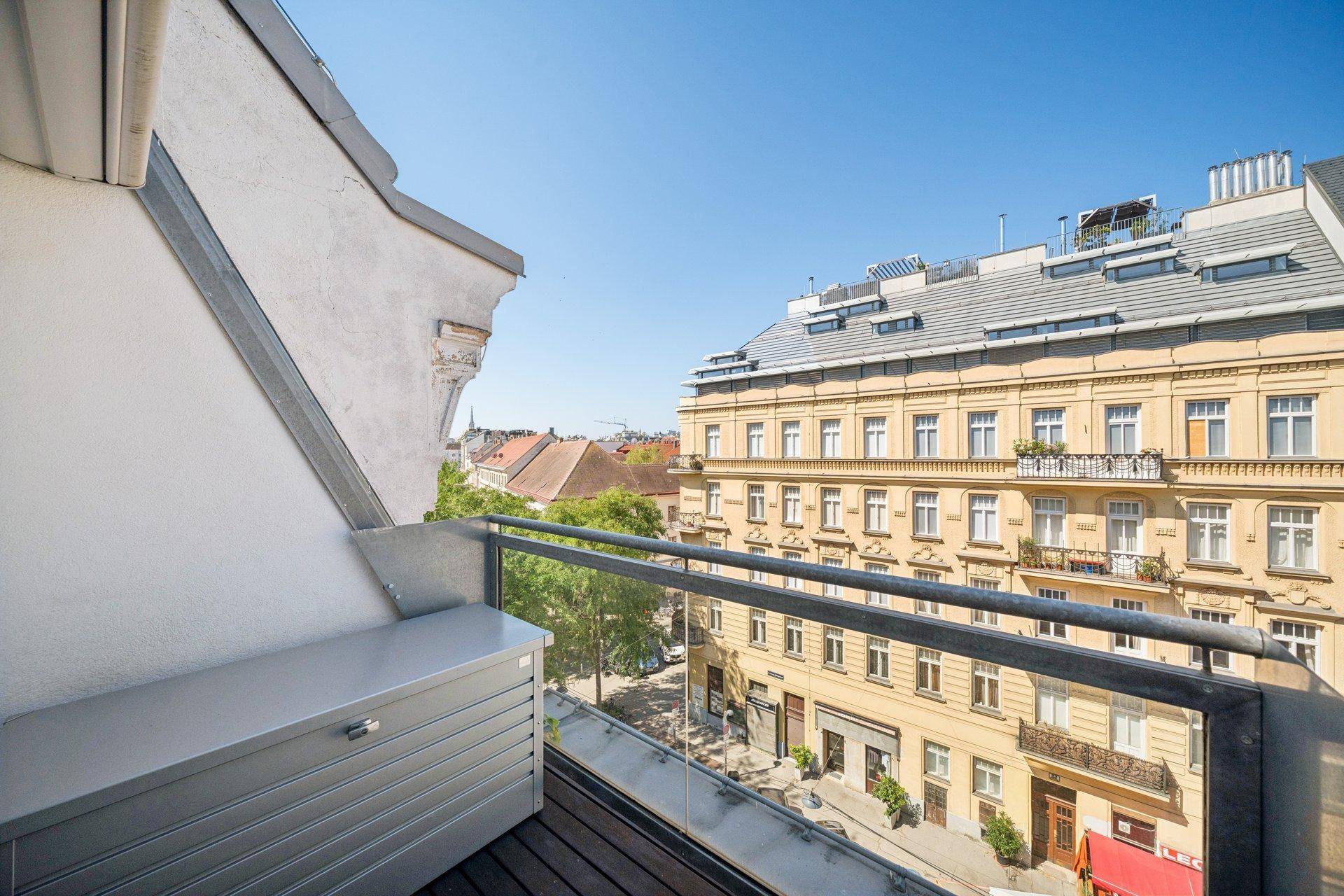 Balkon mit Glasgeländer und Blick auf die belebte Stadtstraße und umliegende Gebäude.