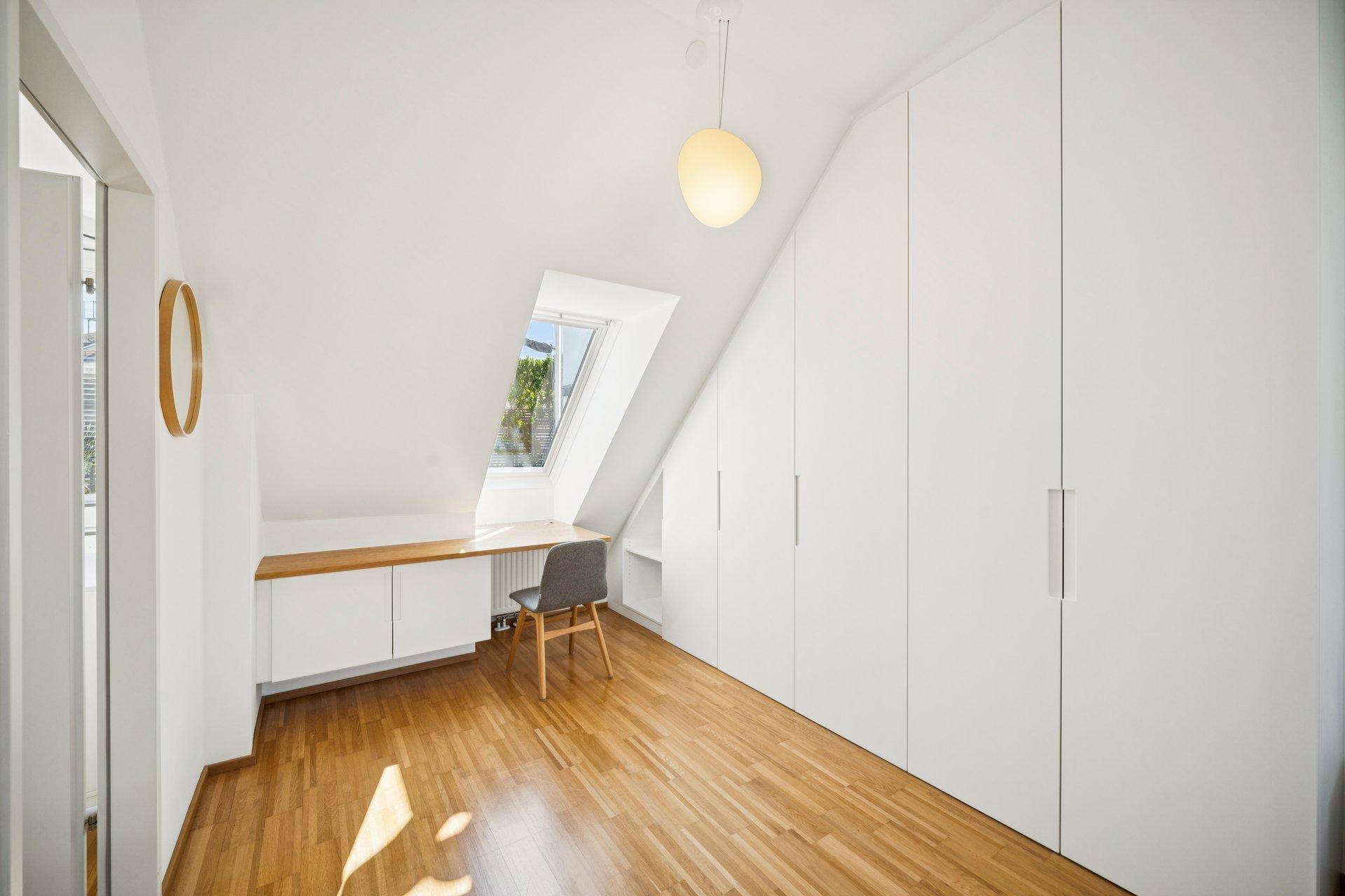 Helles Arbeitszimmer im Dachgeschoss mit Einbauschränken, Schreibtisch und Dachfenster.