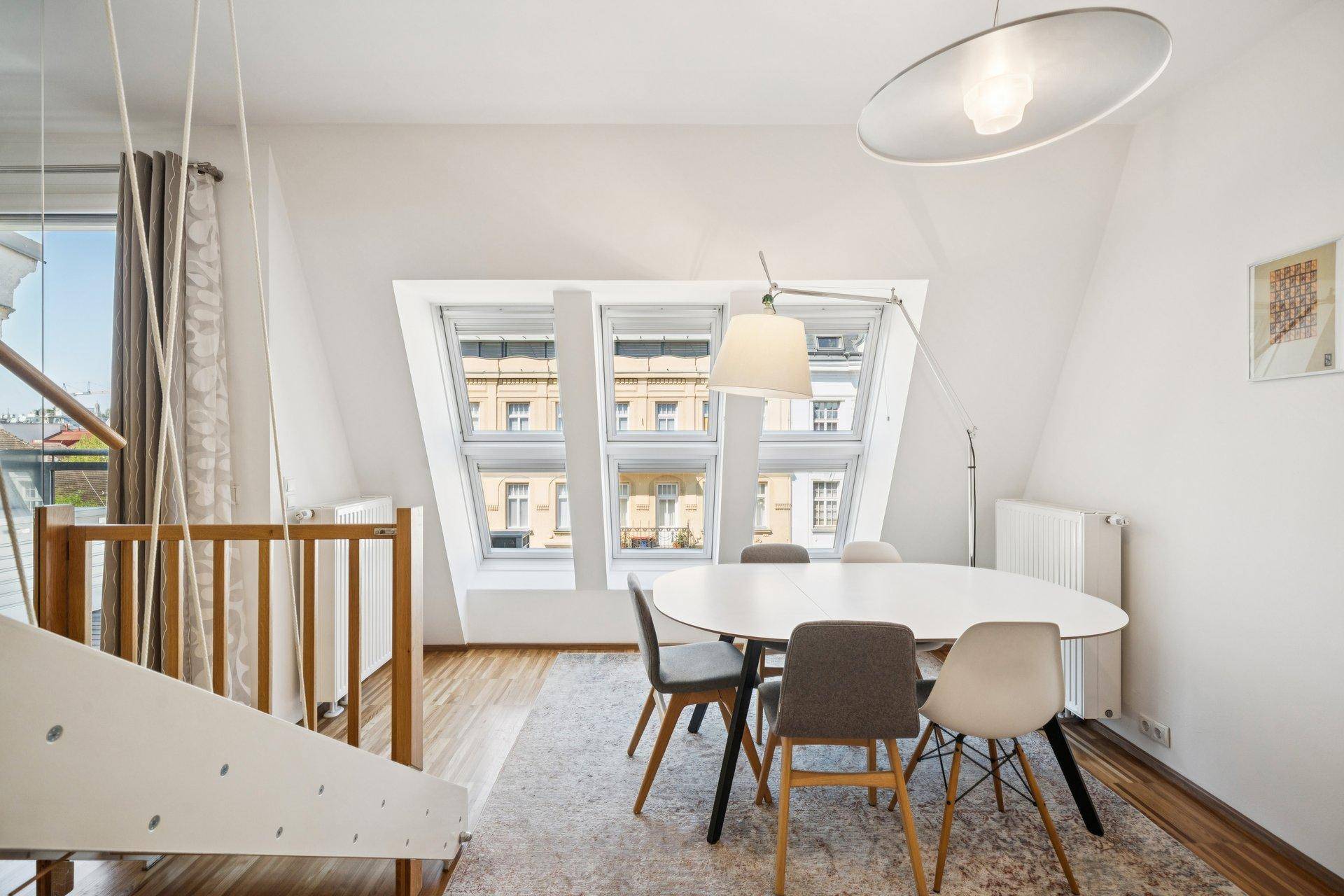Heller Essbereich im Dachgeschoss mit schrägen Wänden, modernen Fenstern und Holzboden.