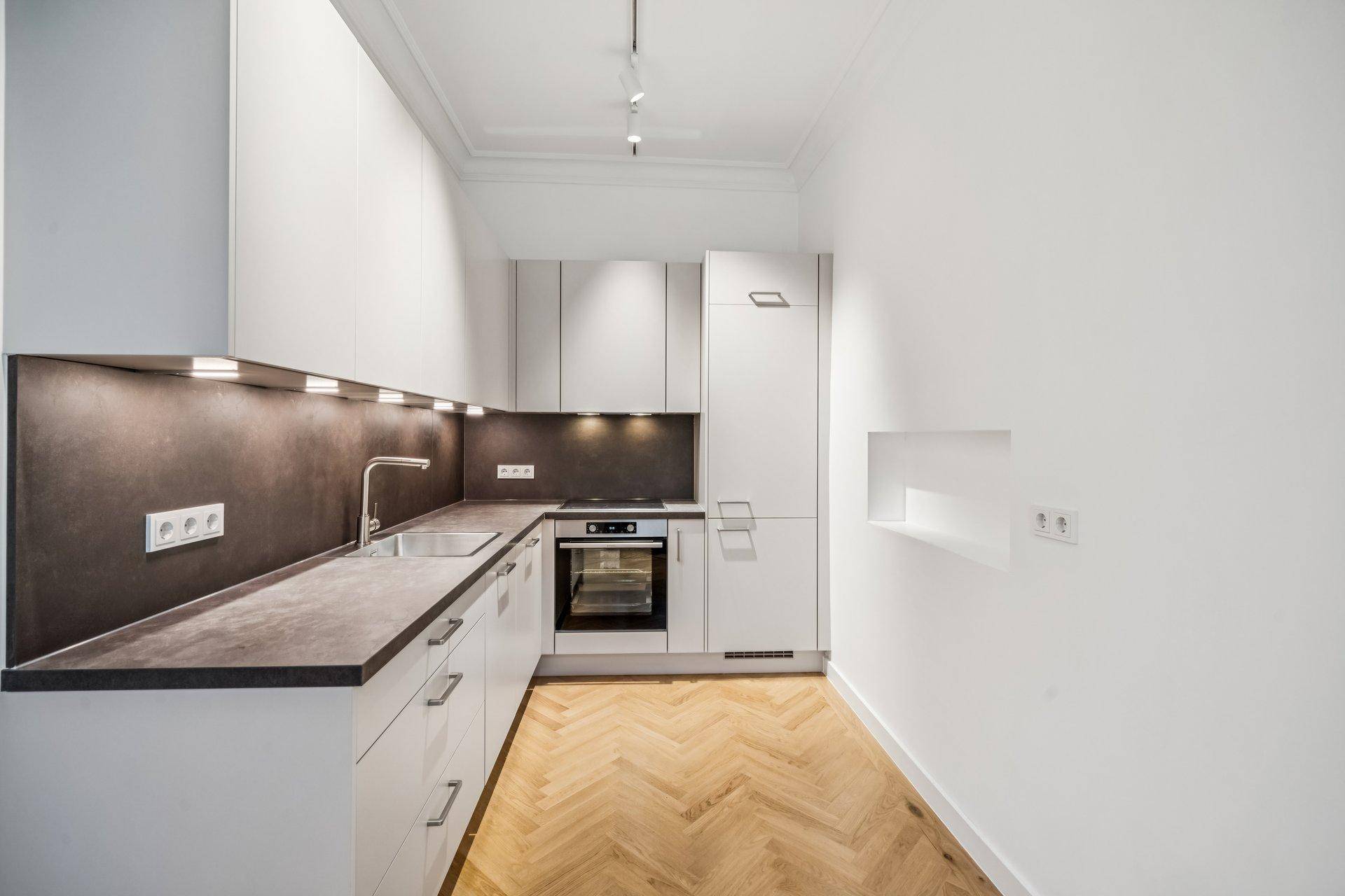 Moderne Küche mit weißen Schränken, dunkler Arbeitsplatte und Fischgrätparkettboden.