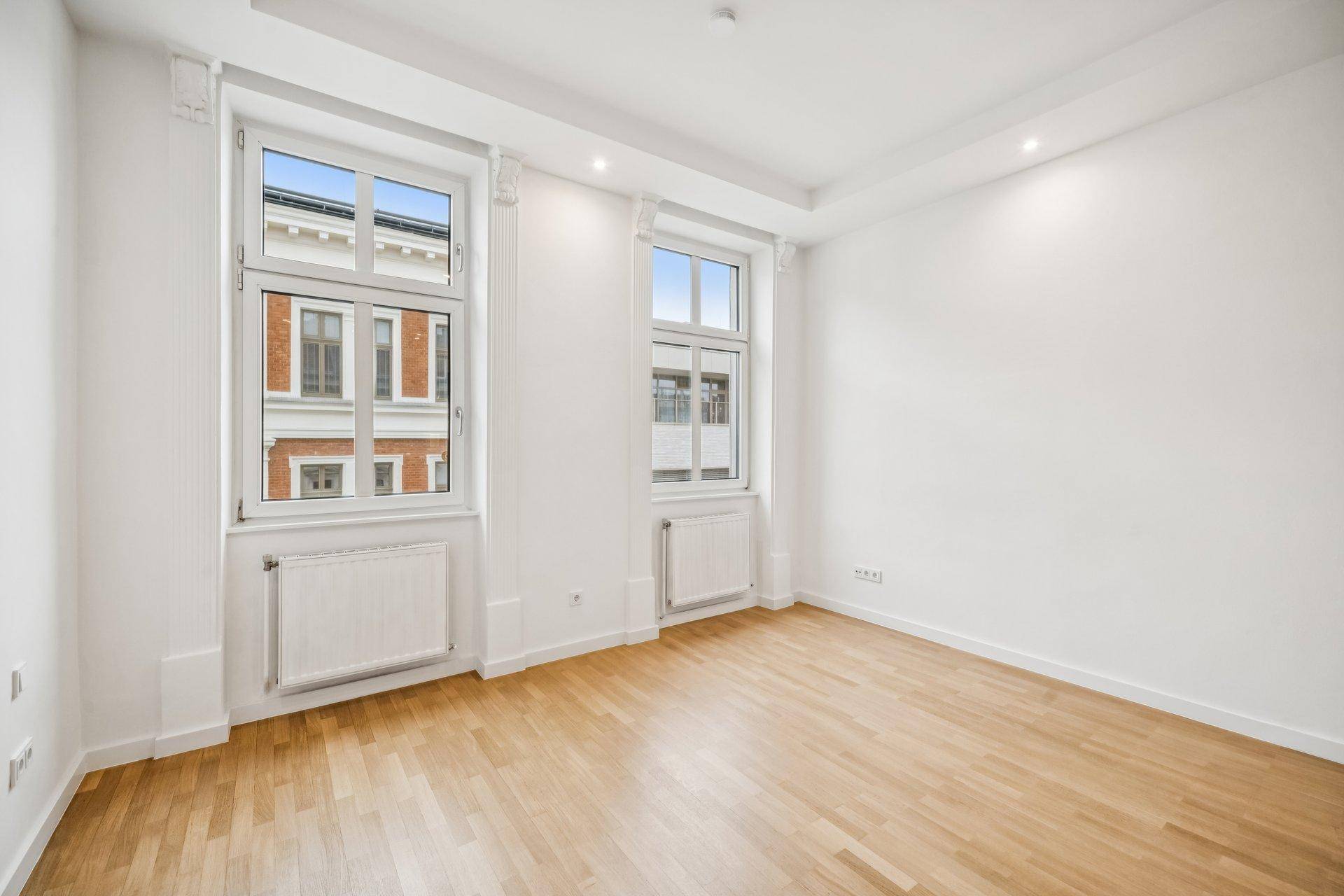 Helles Zimmer mit Parkettboden und zwei großen Fenstern, ideal als Schlaf- oder Arbeitszimmer.