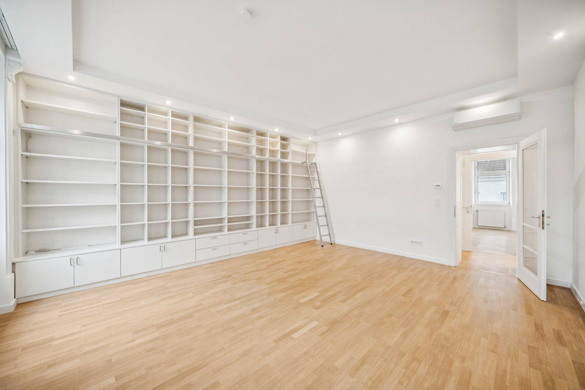 Geräumiges Wohnzimmer mit maßgefertigten Bücherregalen, Parkettboden und Klimaanlage.