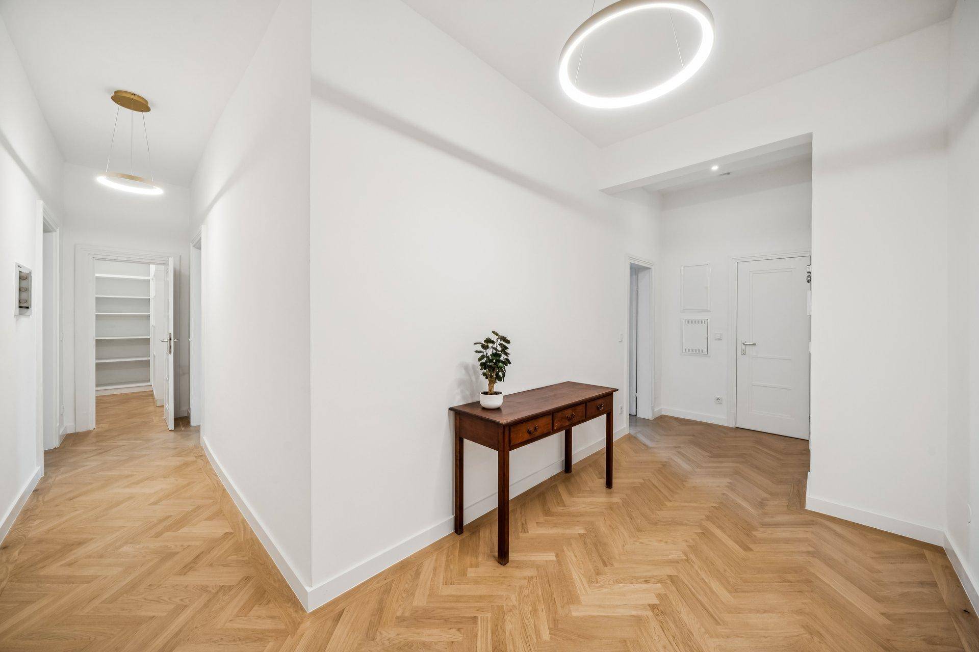 Heller Flur mit Fischgrätparkett, modernen Deckenleuchten und einer eleganten Konsole.