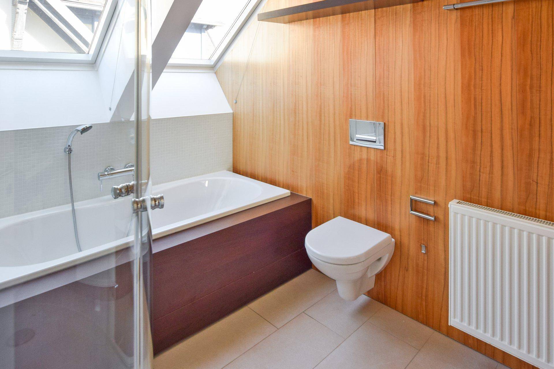 Modernes Badezimmer mit Badewanne, wandhängendem WC und Holzverkleidung unter einem Dachfenster.