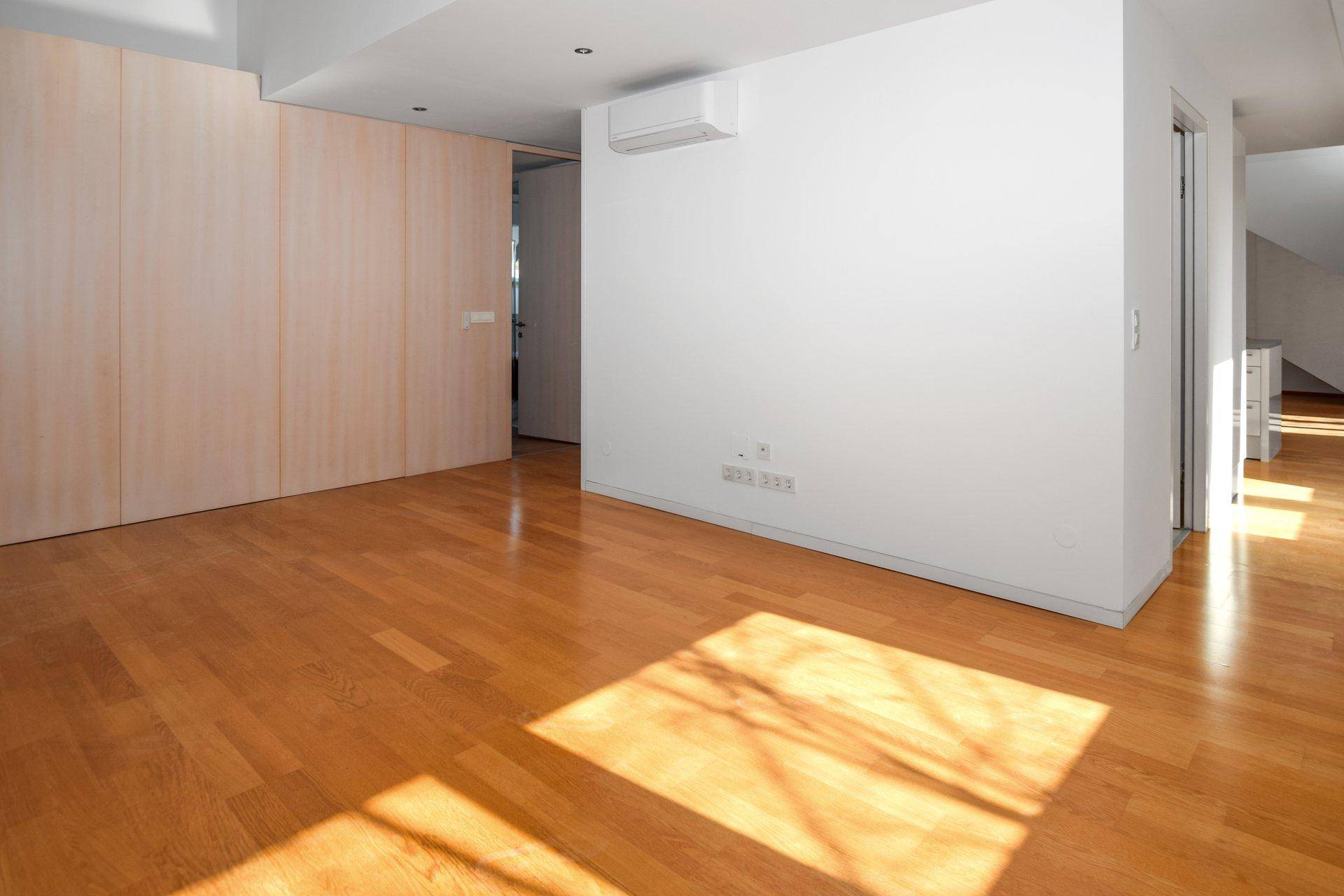 Geräumiges Schlafzimmer mit Holzfußboden, Einbauschränken und Klimaanlage, hell durch Sonnenlicht.