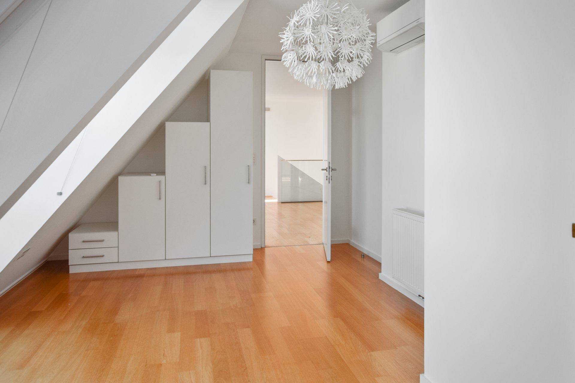 Helles Schlafzimmer mit Holzfußboden und maßgefertigten Einbauschränken unter der Dachschräge.