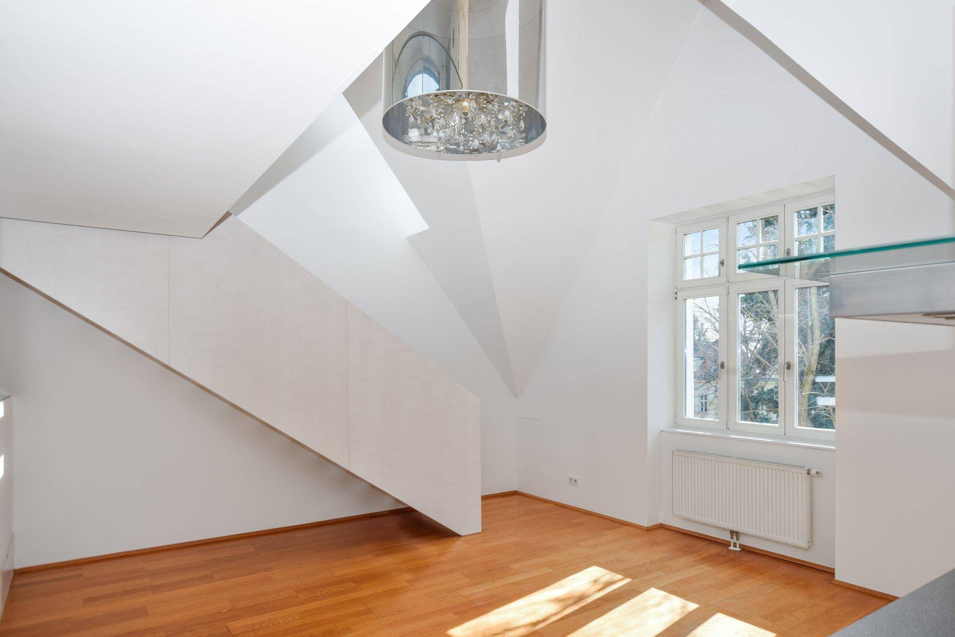 Heller Wohnbereich mit Holzfußboden, moderner Treppe und einem großen Fenster, das viel Licht spendet.