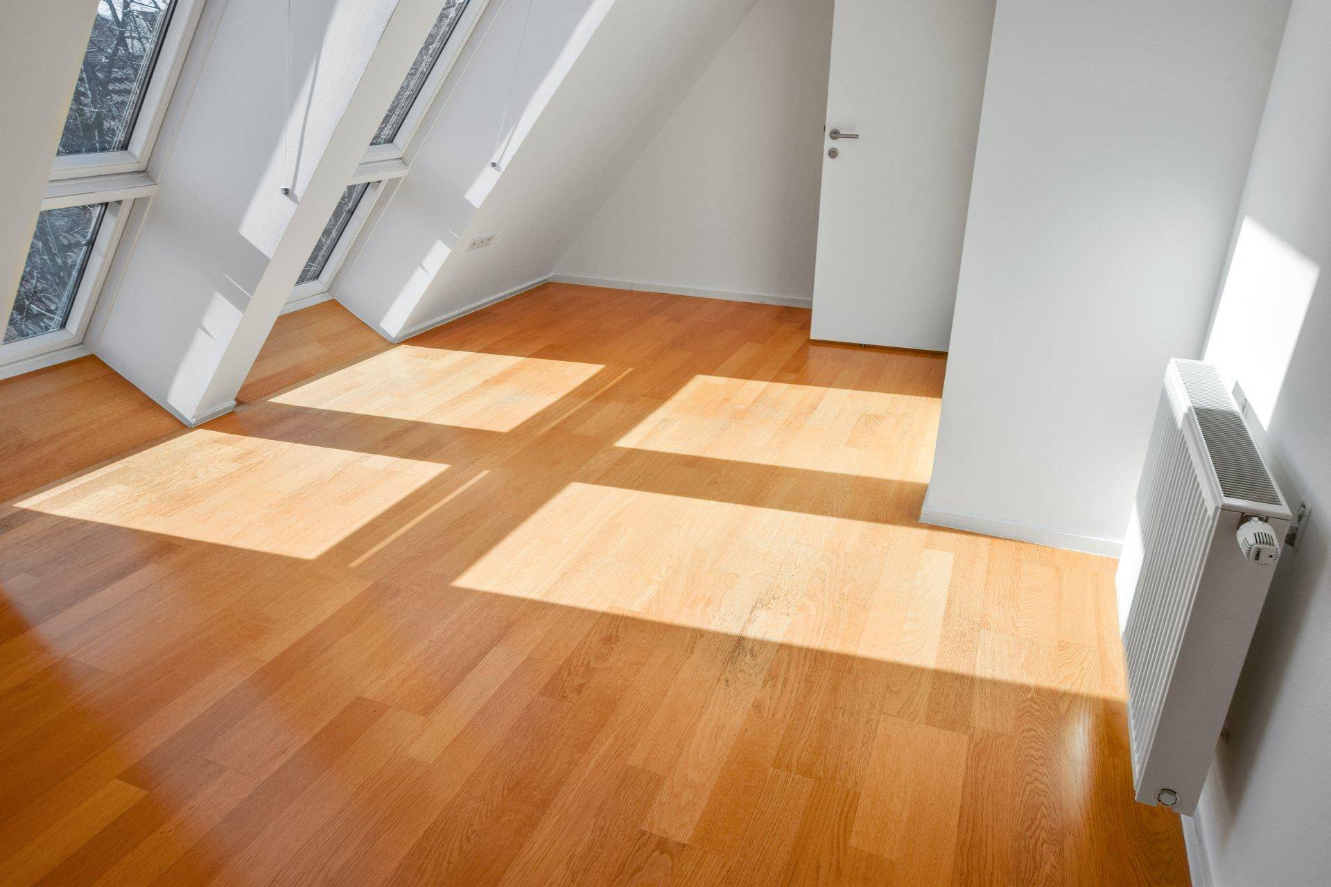 Helles Zimmer im Dachgeschoss mit Holzfußboden und mehreren Dachfenstern, die den Raum sonnig machen.