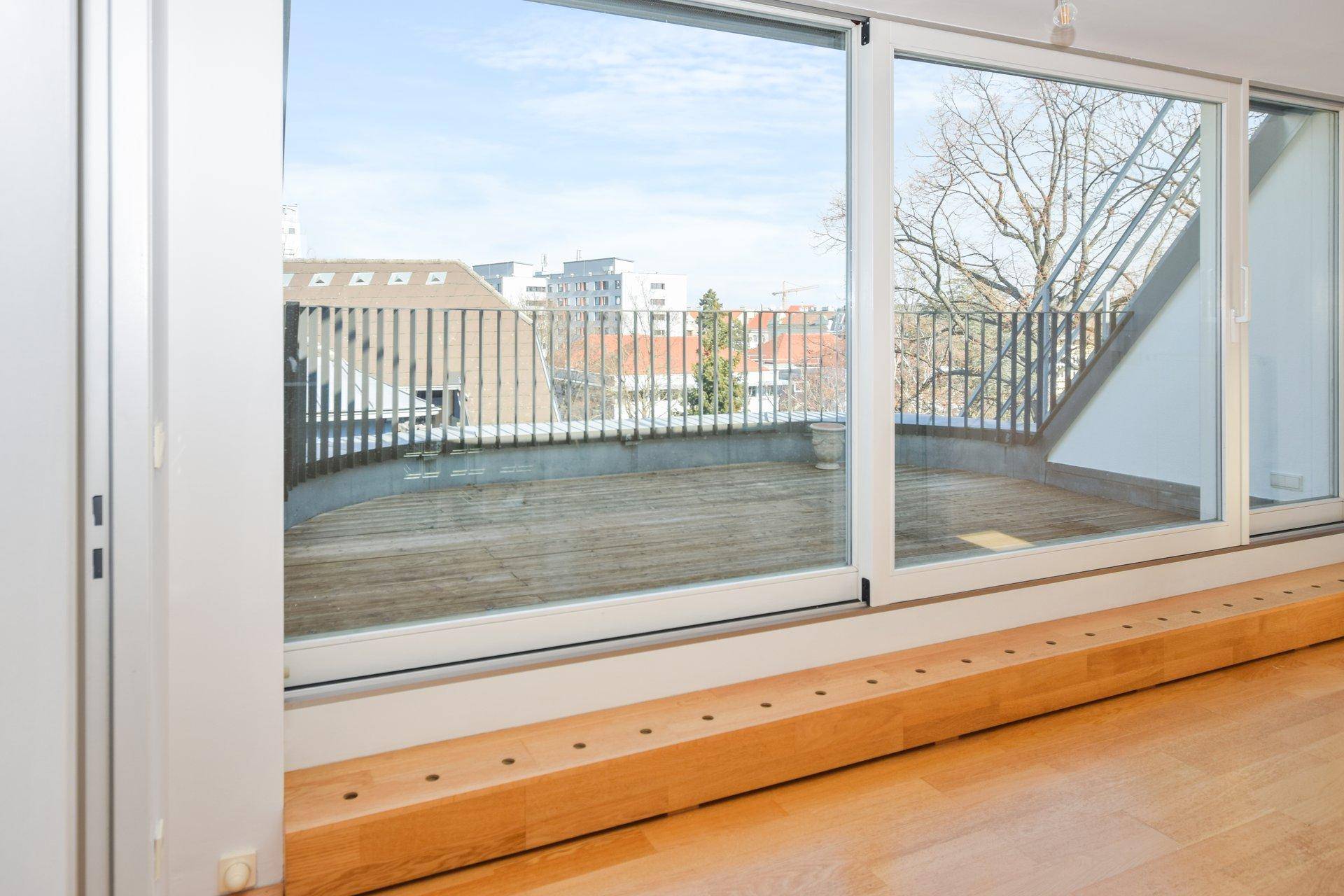 Heller Innenraum mit großen Schiebetüren, die auf eine Dachterrasse führen und viel Tageslicht hereinlassen.