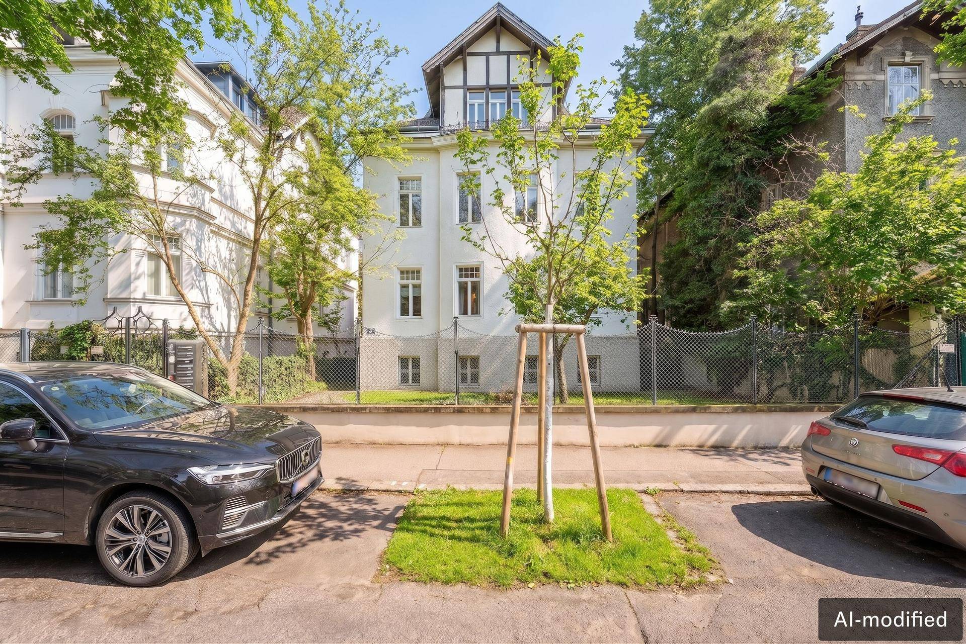 Klassische Stadtvilla mit weißer Fassade und grüner Umgebung, geparkt sind Autos auf der Straße.