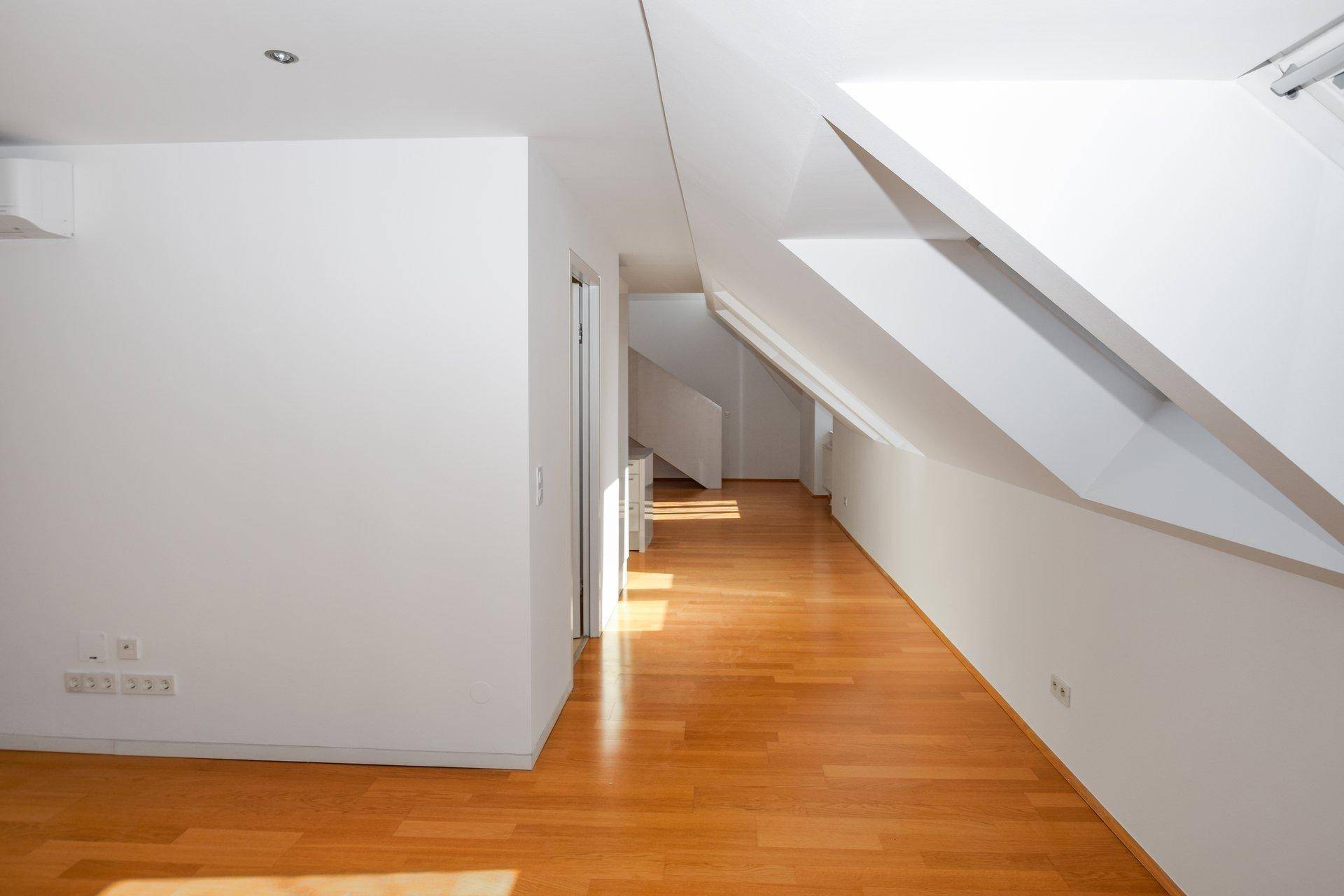 Heller Flur mit Holzfußboden und schrägen Wänden, der zu weiteren Räumen und einer Treppe führt.