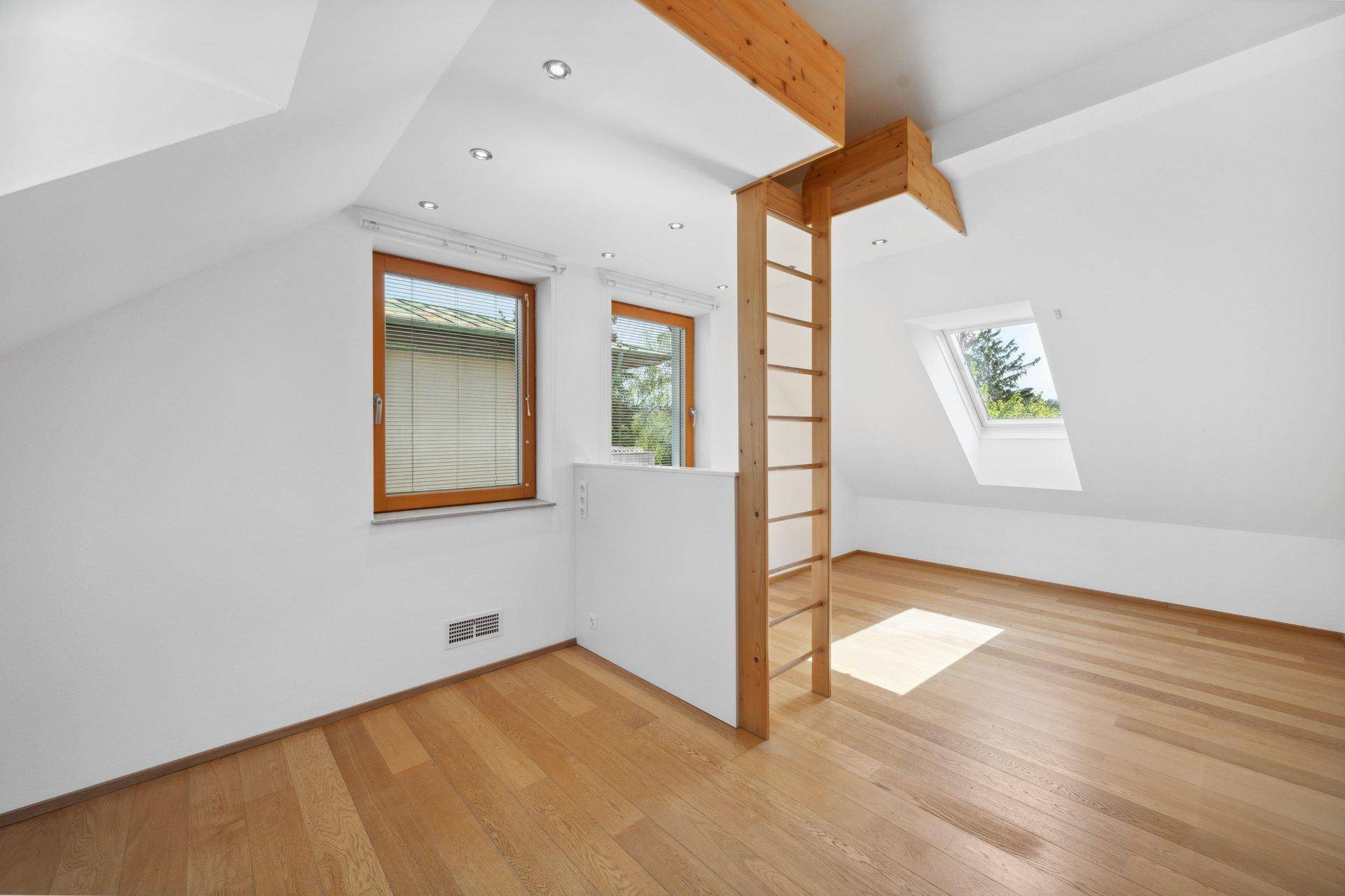 Helles Dachzimmer mit Holzboden, Dachfenster und einer Holzleiter zu einer oberen Ebene.