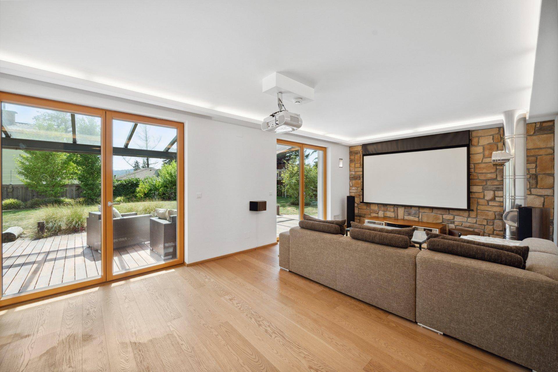 Gemütliches Wohnzimmer mit Projektor, Leinwand, Steinfassade und Zugang zum Garten.