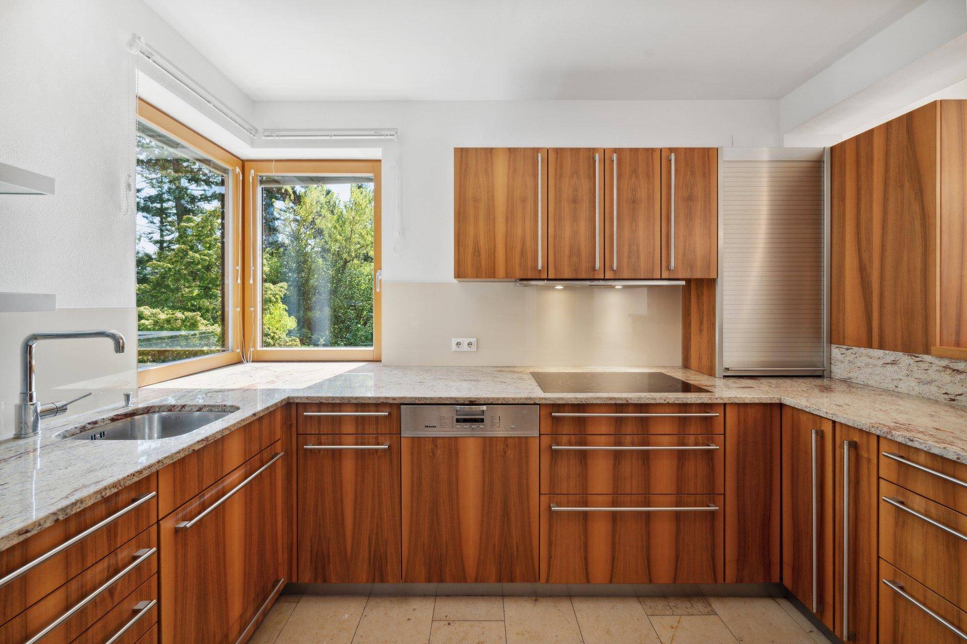 Moderne Holzküche mit Granitarbeitsplatten, Einbaugeräten und Fenster mit Waldblick.