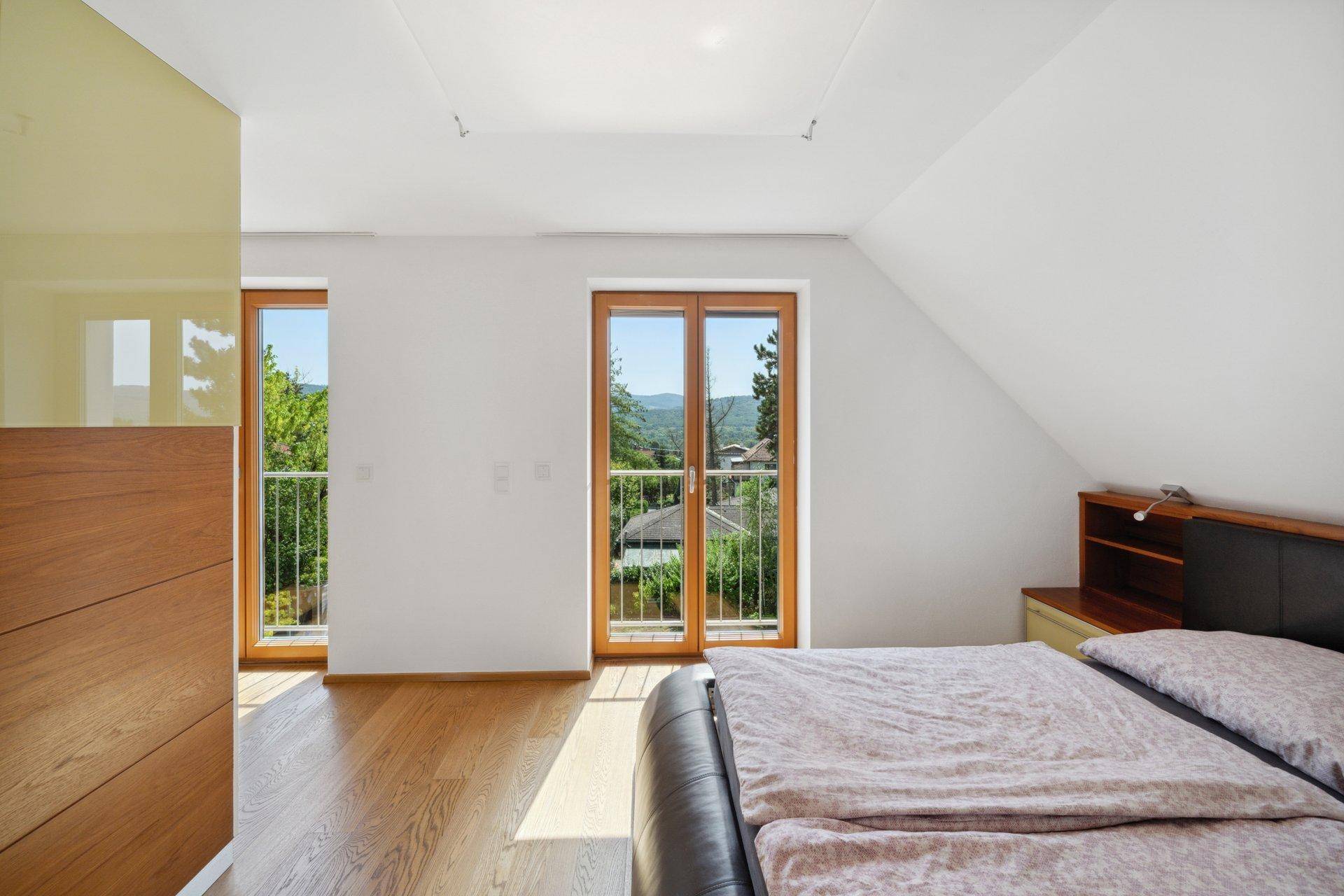 Schlafzimmer im Dachgeschoss mit Holzboden, französischem Balkon und Blick ins Grüne.