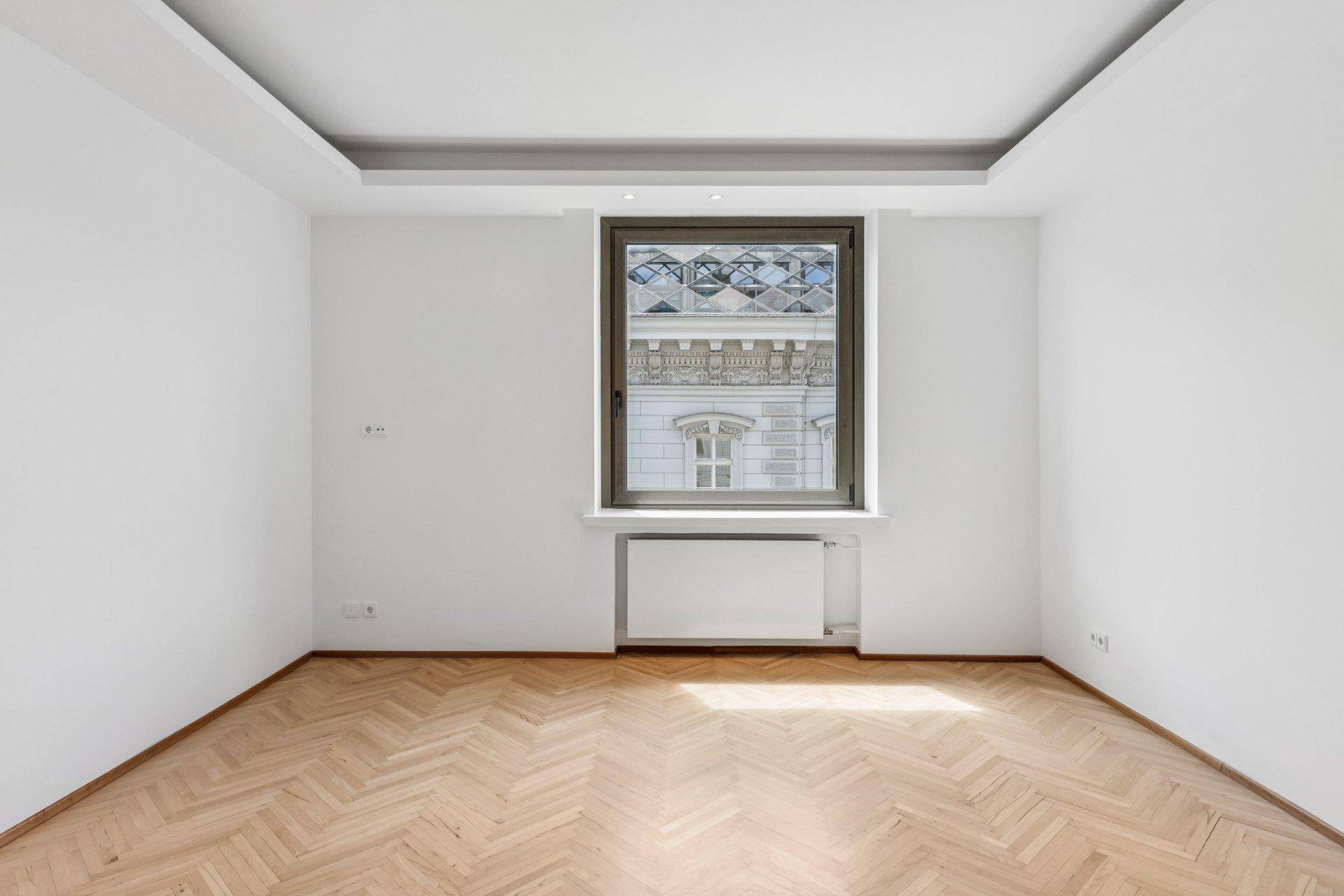 Heller, leerer Raum mit Fischgrätparkett und Blick auf die Stadt.