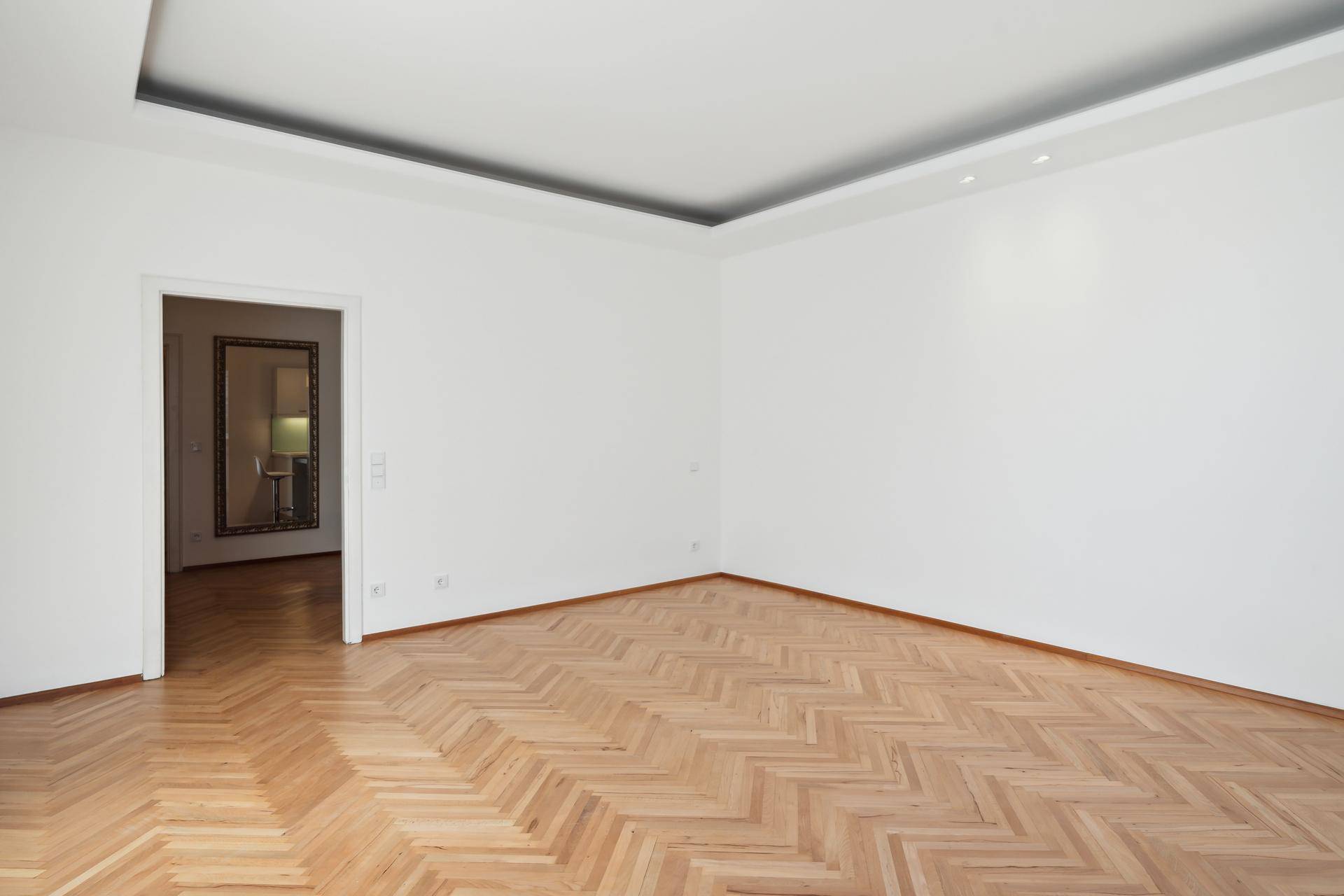 Leerer Raum mit Fischgrätparkett und Zugang zu einem weiteren Zimmer.