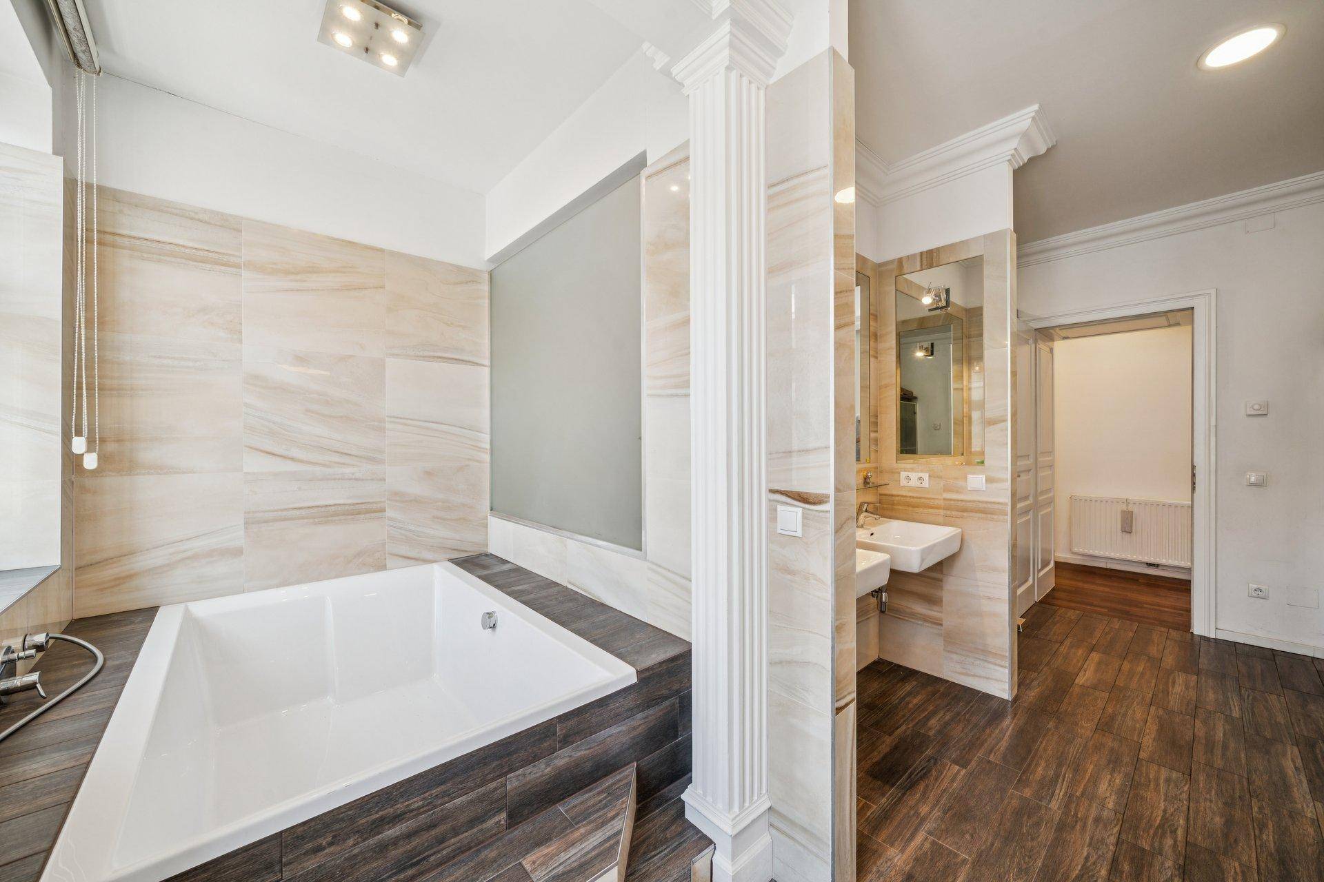 Geräumiges Badezimmer mit großer Badewanne, eleganten Fliesen und modernem Waschtischbereich.