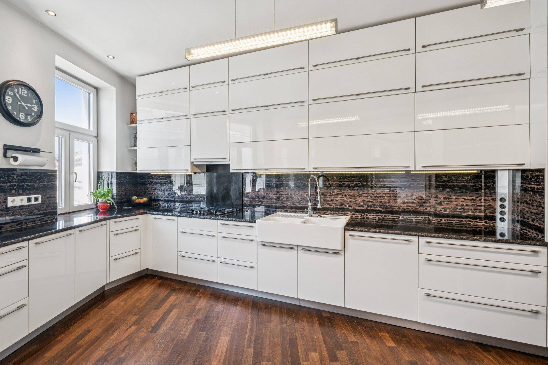 Elegante Einbauküche mit glänzenden weißen Schränken, dunkler Granitplatte und Spülbecken.