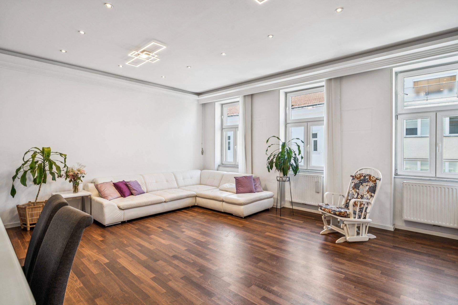 Geräumiges Wohnzimmer mit bequemer Eckcouch, Holzboden und großen Fenstern für viel Tageslicht.