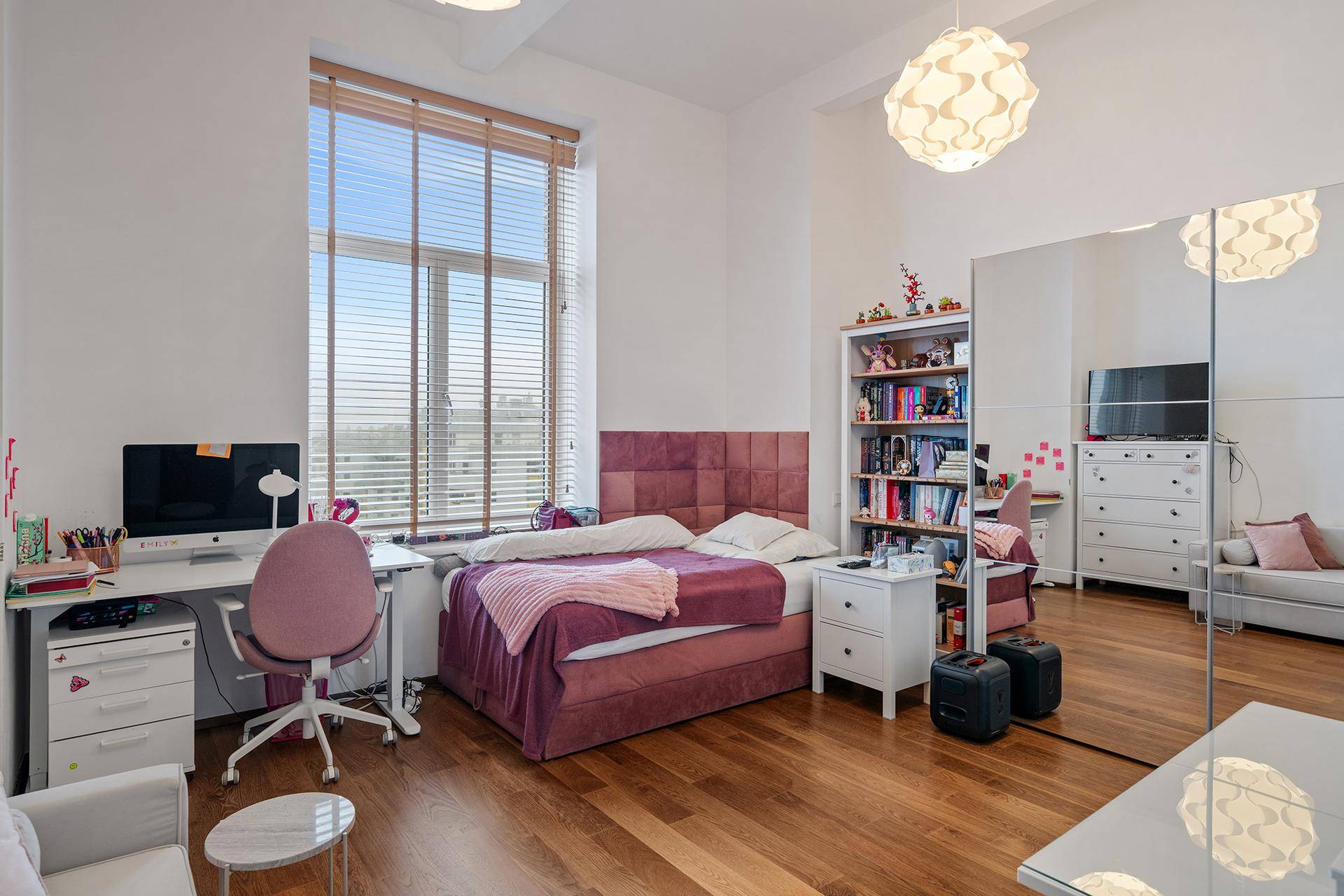 Jugendzimmer mit Holzboden, großem Fenster, Schreibtisch und Spiegelschrank.