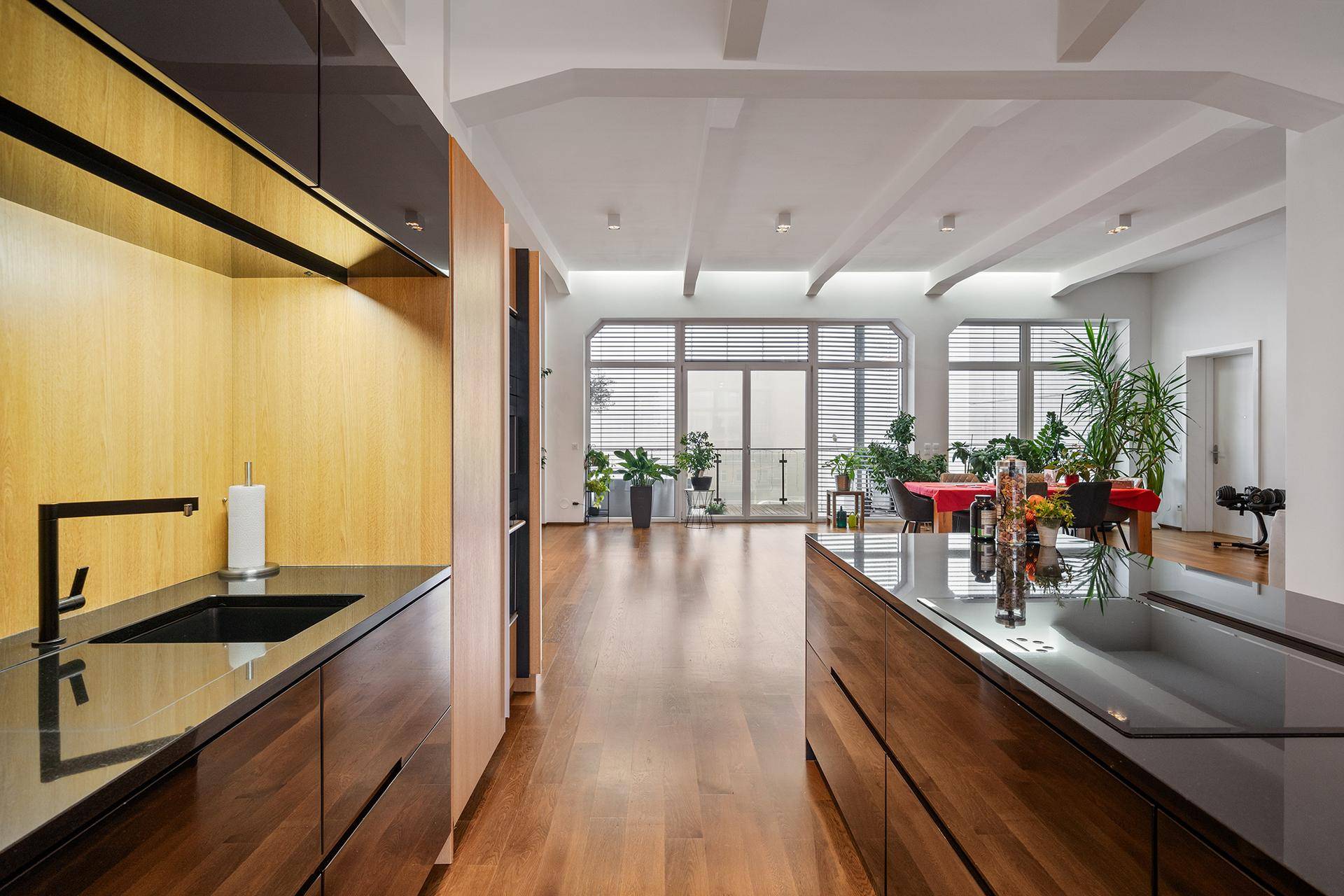 Moderne Küche mit dunklen Holzfronten, schwarzer Arbeitsplatte und Blick in den offenen Wohnbereich.