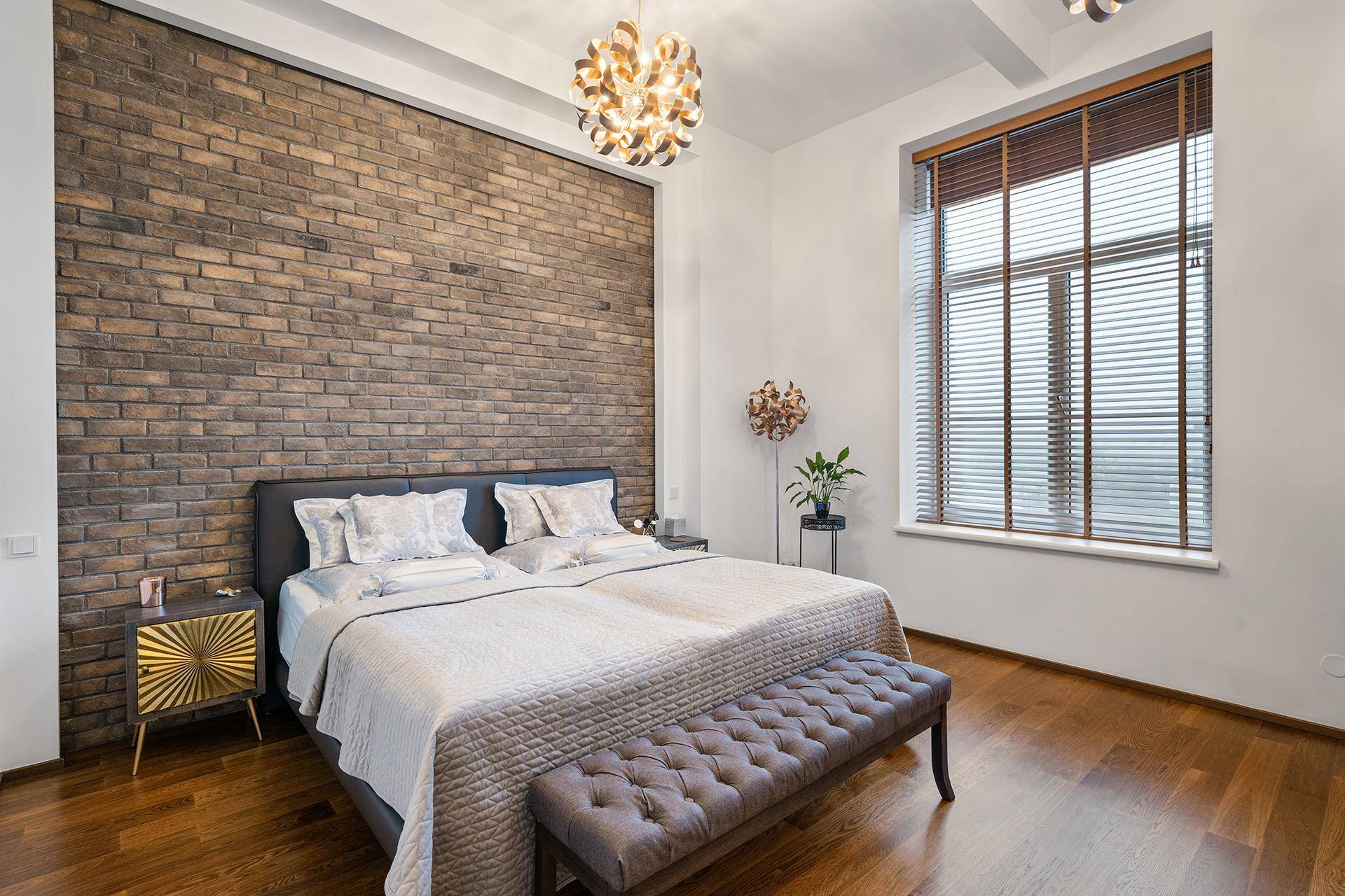 Schlafzimmer mit Akzentwand aus Ziegeln, Holzboden und modernem Deckenlicht.