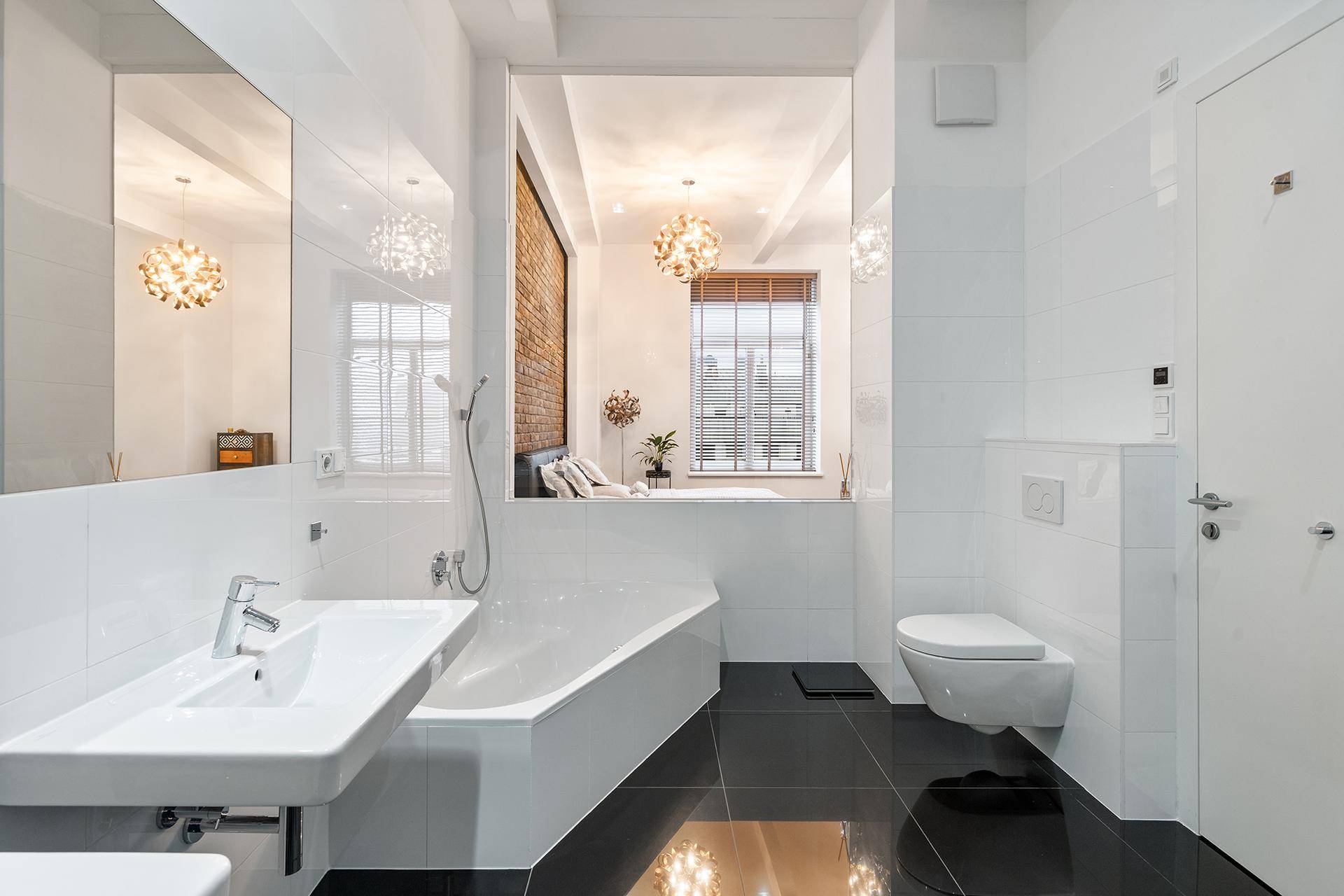 Modernes Badezimmer mit weißen Fliesen, schwarzem Boden und Badewanne mit Blick ins Schlafzimmer.