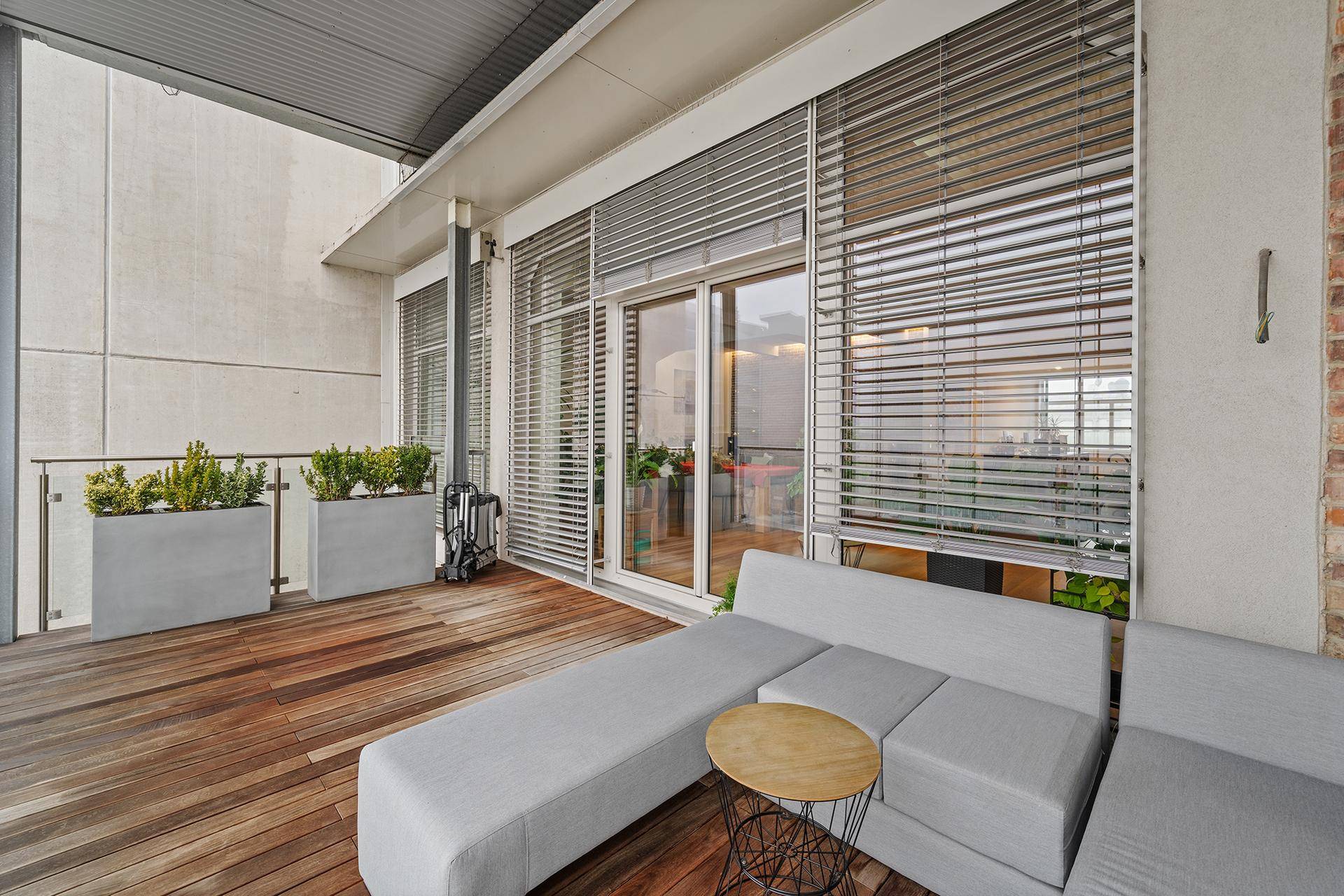 Großer Balkon mit Holzboden, bequemen Loungemöbeln und Pflanzen in modernen Pflanzkübeln.