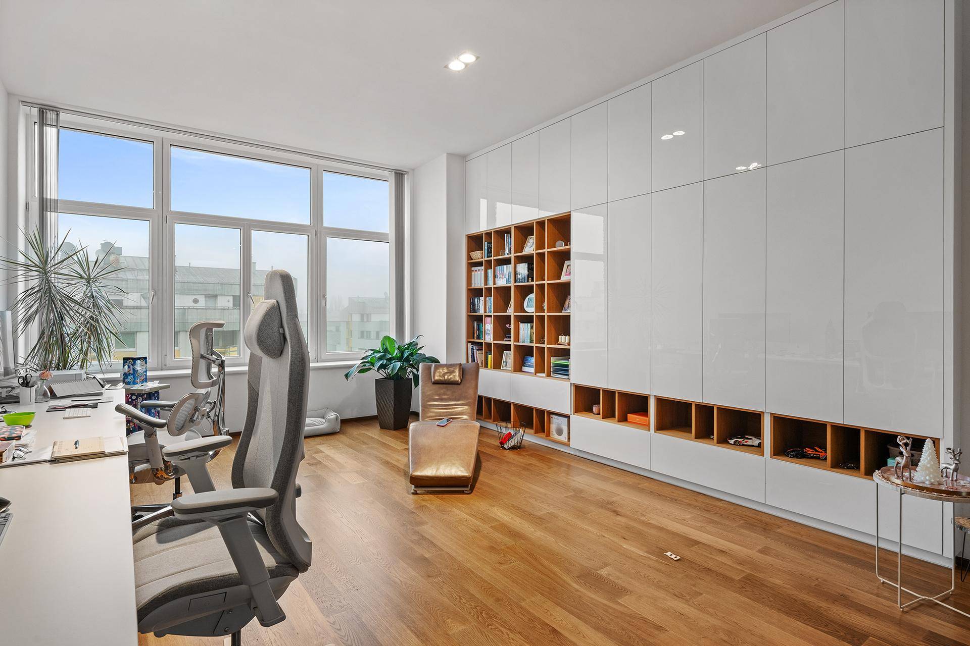 Helles Büro mit großen Fenstern, Holzboden und integrierten weißen Schränken.