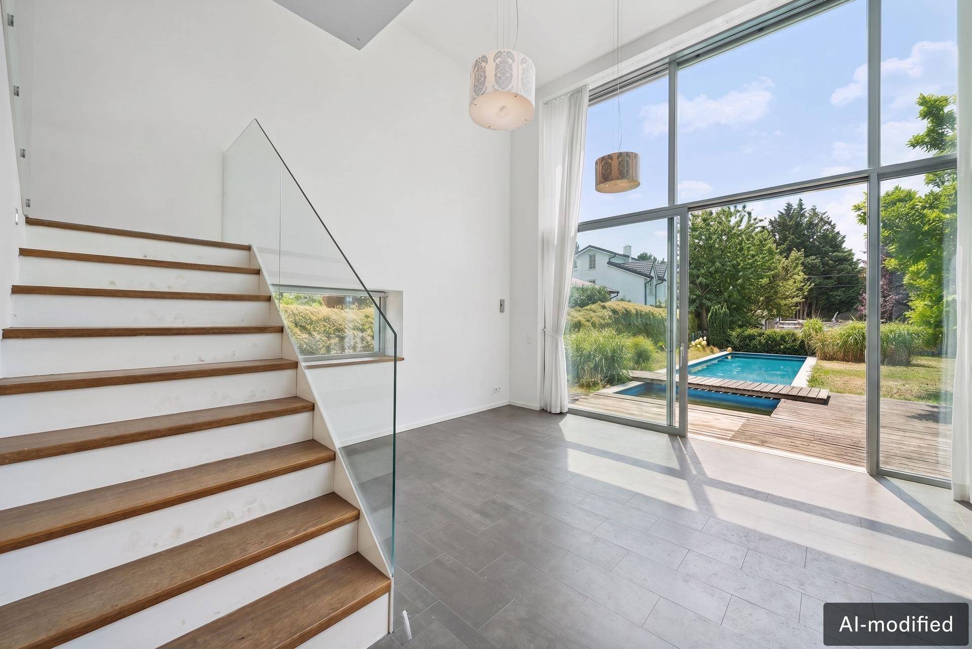 Heller Eingangsbereich mit moderner Treppe, Glasgeländer und großen Fenstern zum Poolbereich.