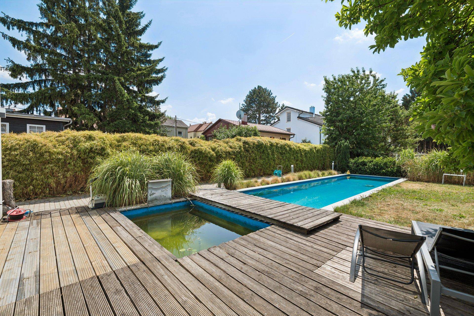 Großer Gartenbereich mit Holzdeck, Schwimmbecken und Biotop, umgeben von üppigem Grün.