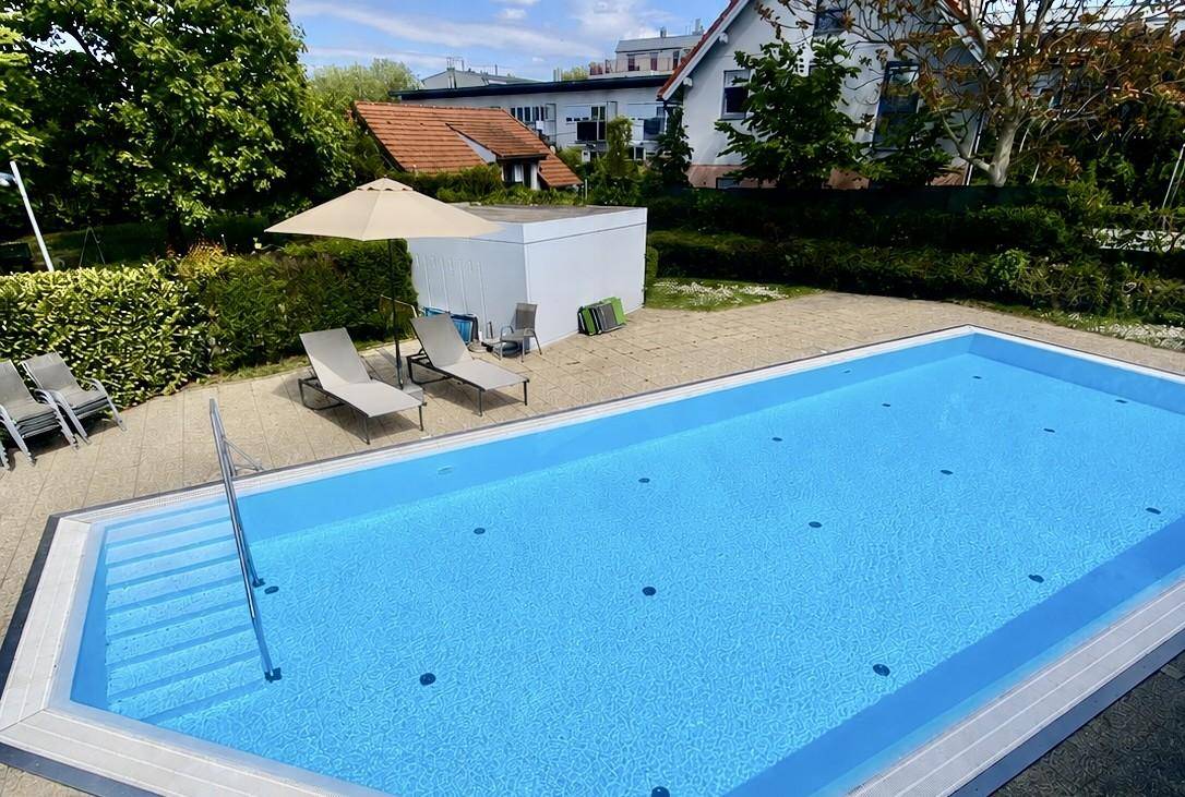 Außenpoolbereich mit Liegestühlen und umgebender Grünfläche.