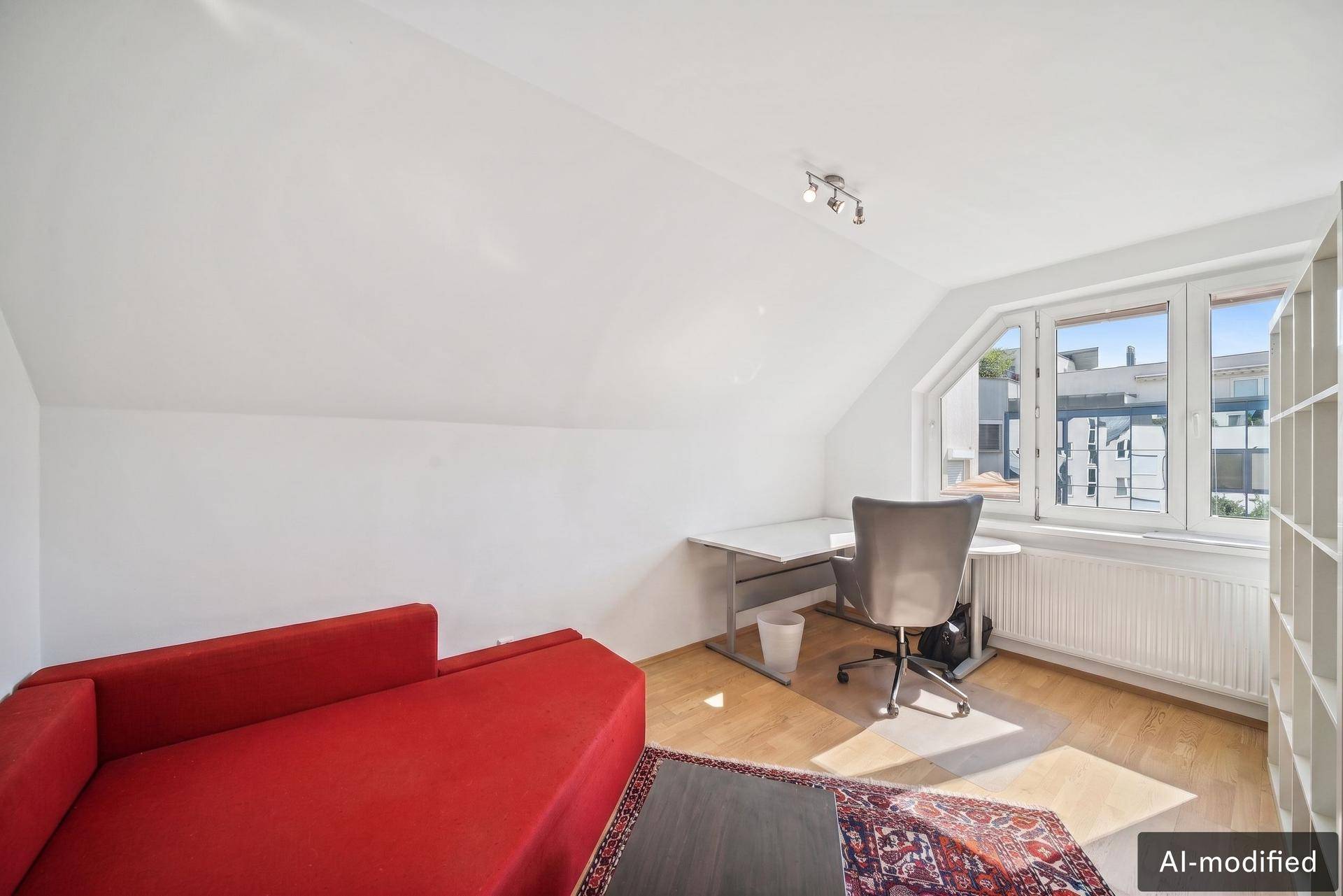 Freundliches Zimmer mit Holzboden, Schreibtisch und rotem Sofa unter Dachschräge.
