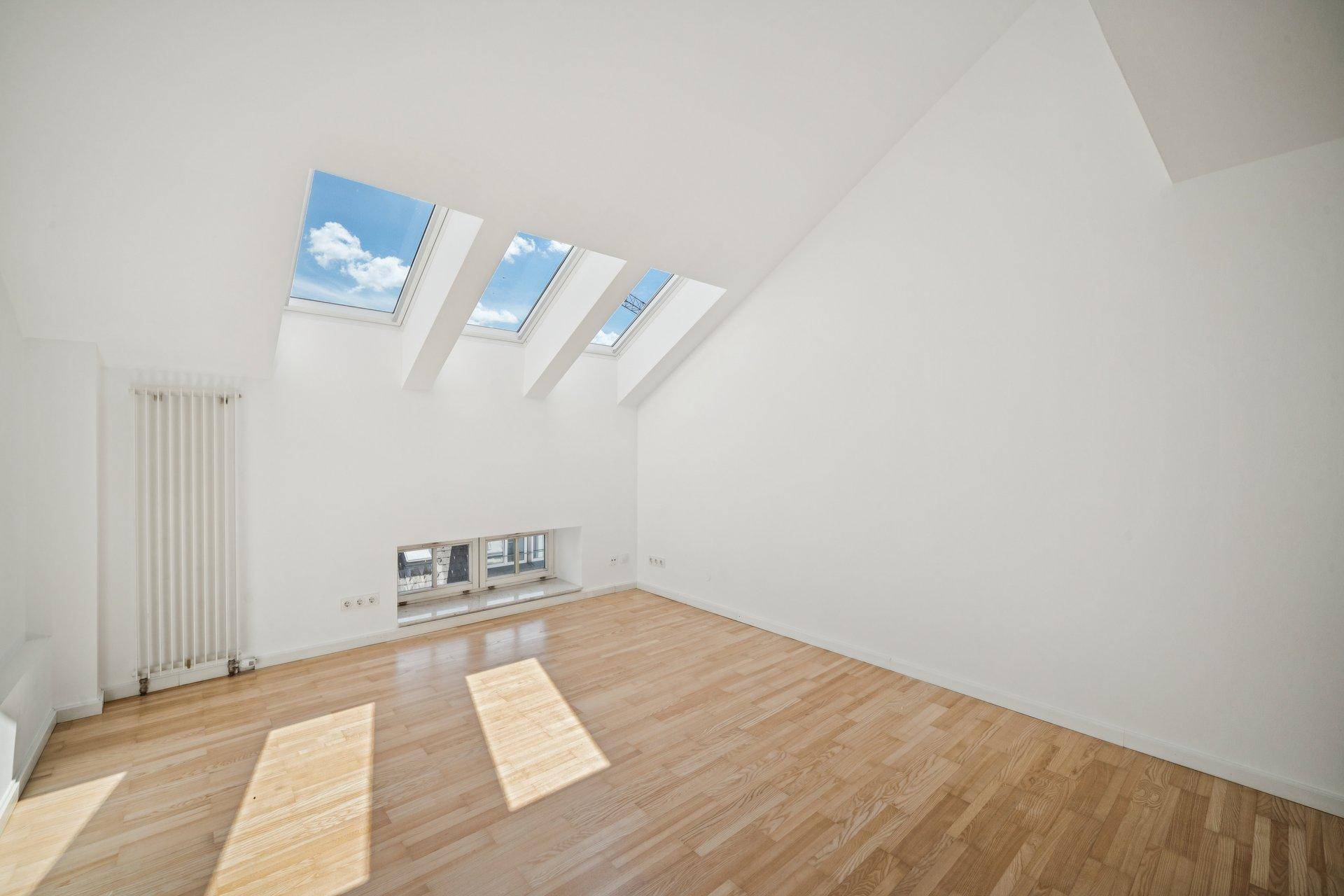 Leerer Raum im Dachgeschoss mit Holzboden, Heizkörper und mehreren Dachfenstern.