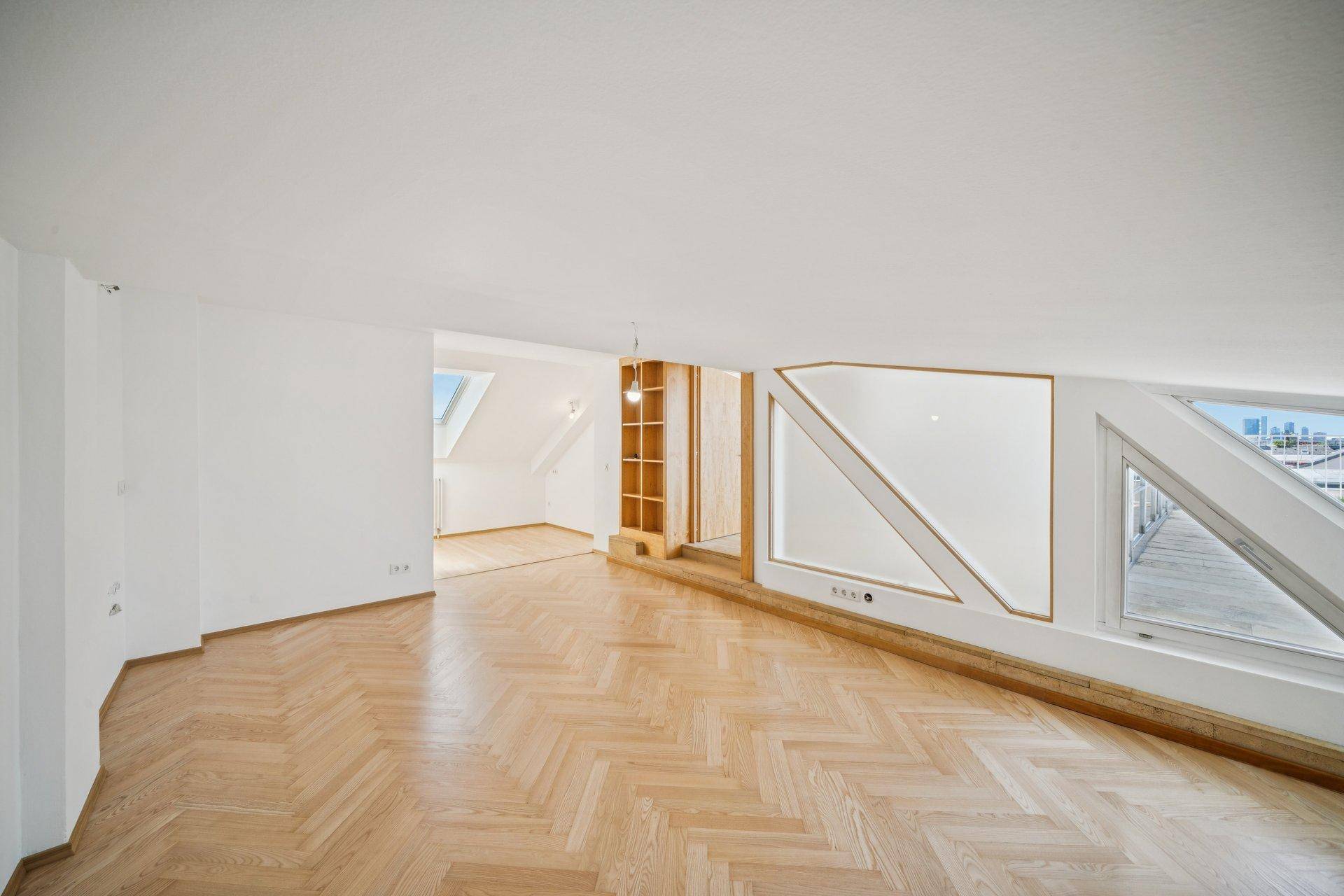 Großer, heller Raum mit Fischgrätparkett und schrägen Wänden im Dachgeschoss.