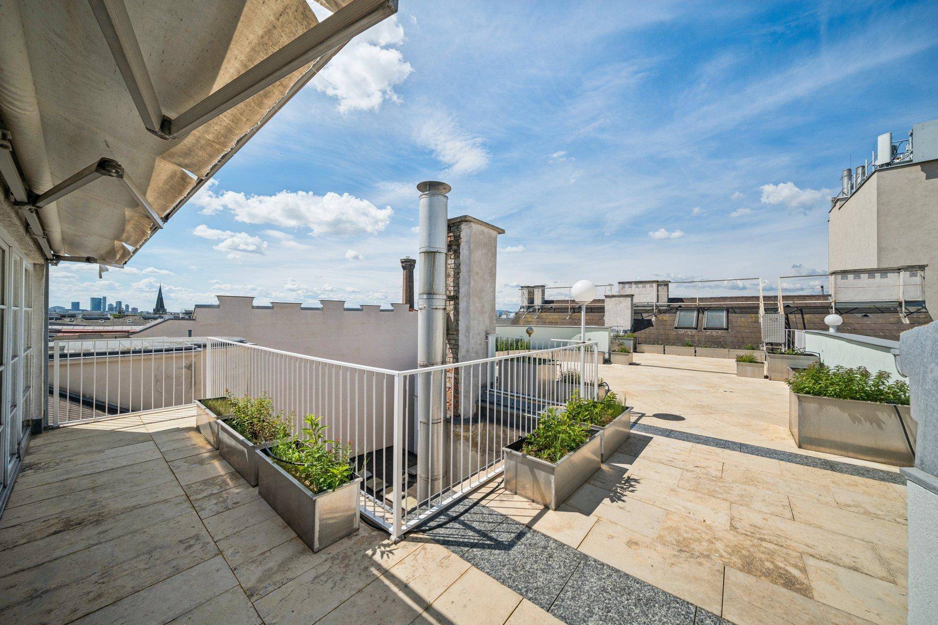 Sonniger Terrassenbereich auf dem Dach mit Blick über die Stadt und umliegende Gebäude.