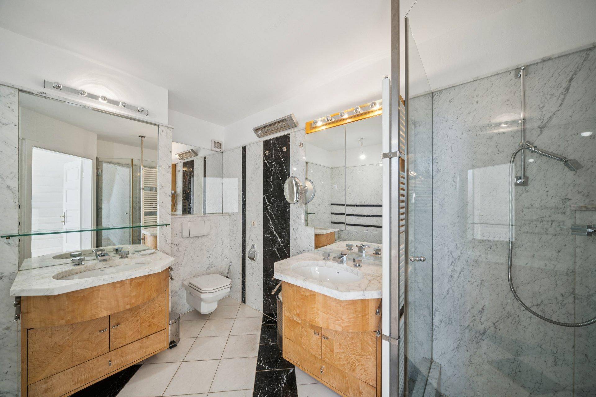 Elegantes Badezimmer mit Marmoroberflächen, Doppelwaschbecken und moderner Duschkabine.