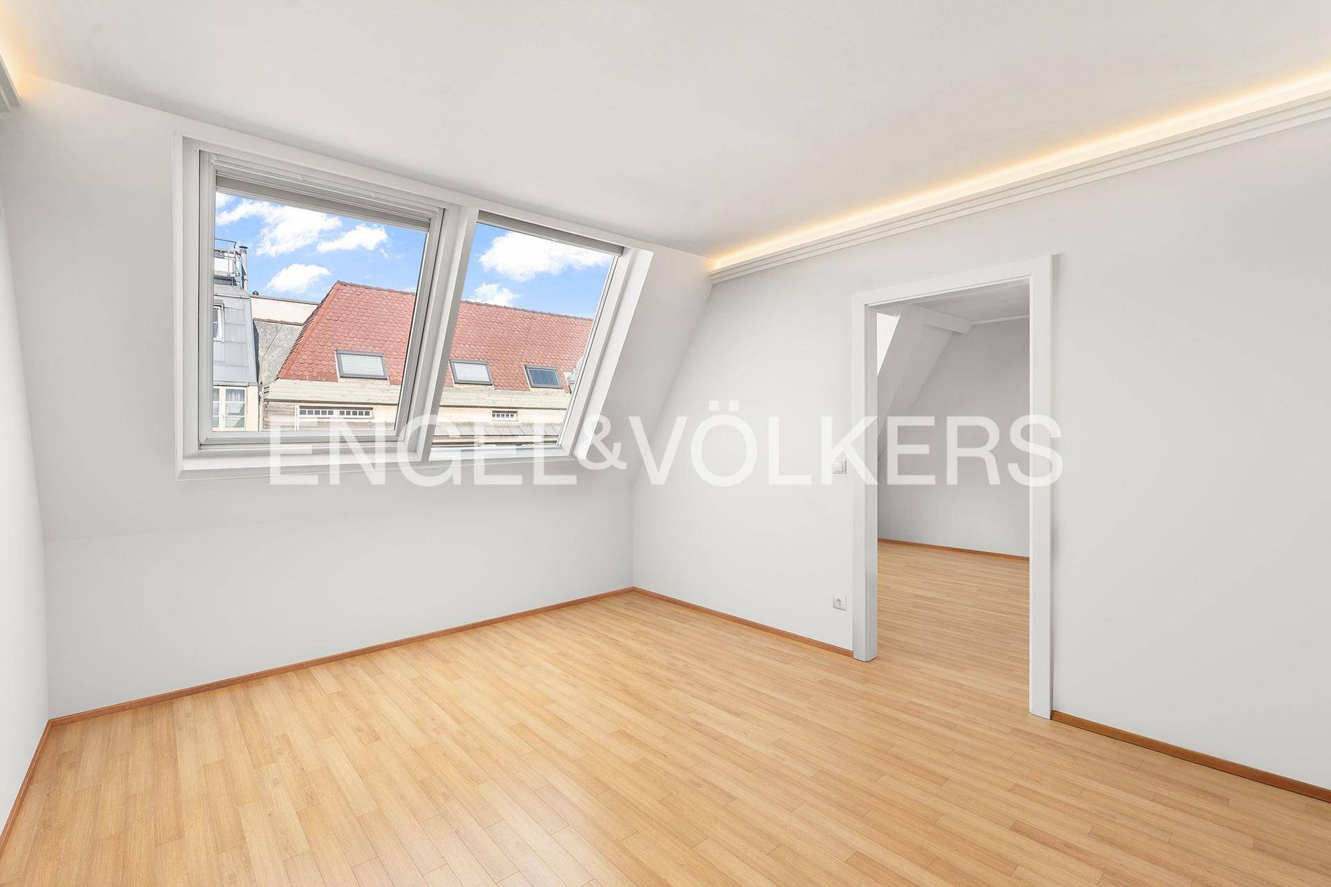 Leeres Zimmer im Dachgeschoss mit schrägen Wänden, Fenster und hellem Holzboden.