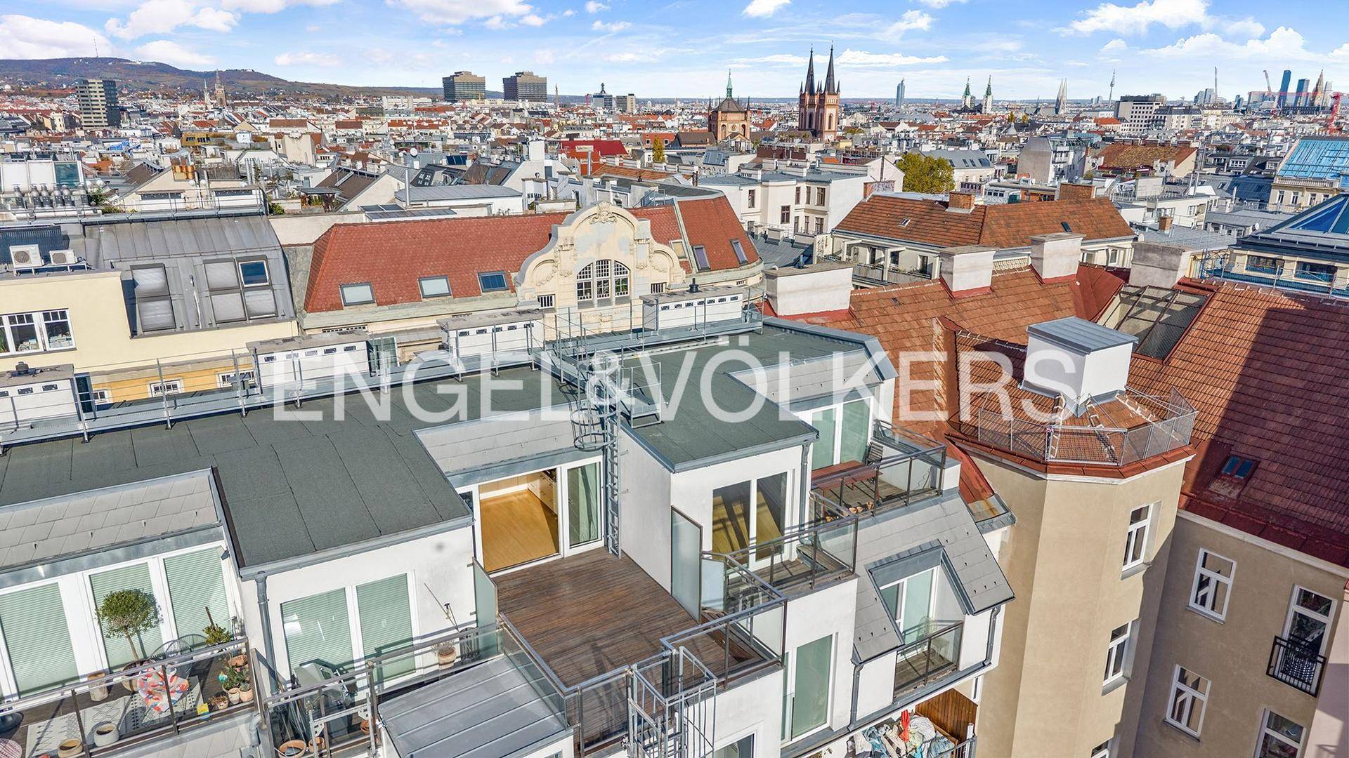 Luftaufnahme eines modernen Gebäudes mit mehreren Terrassen und Blick auf die Stadt.