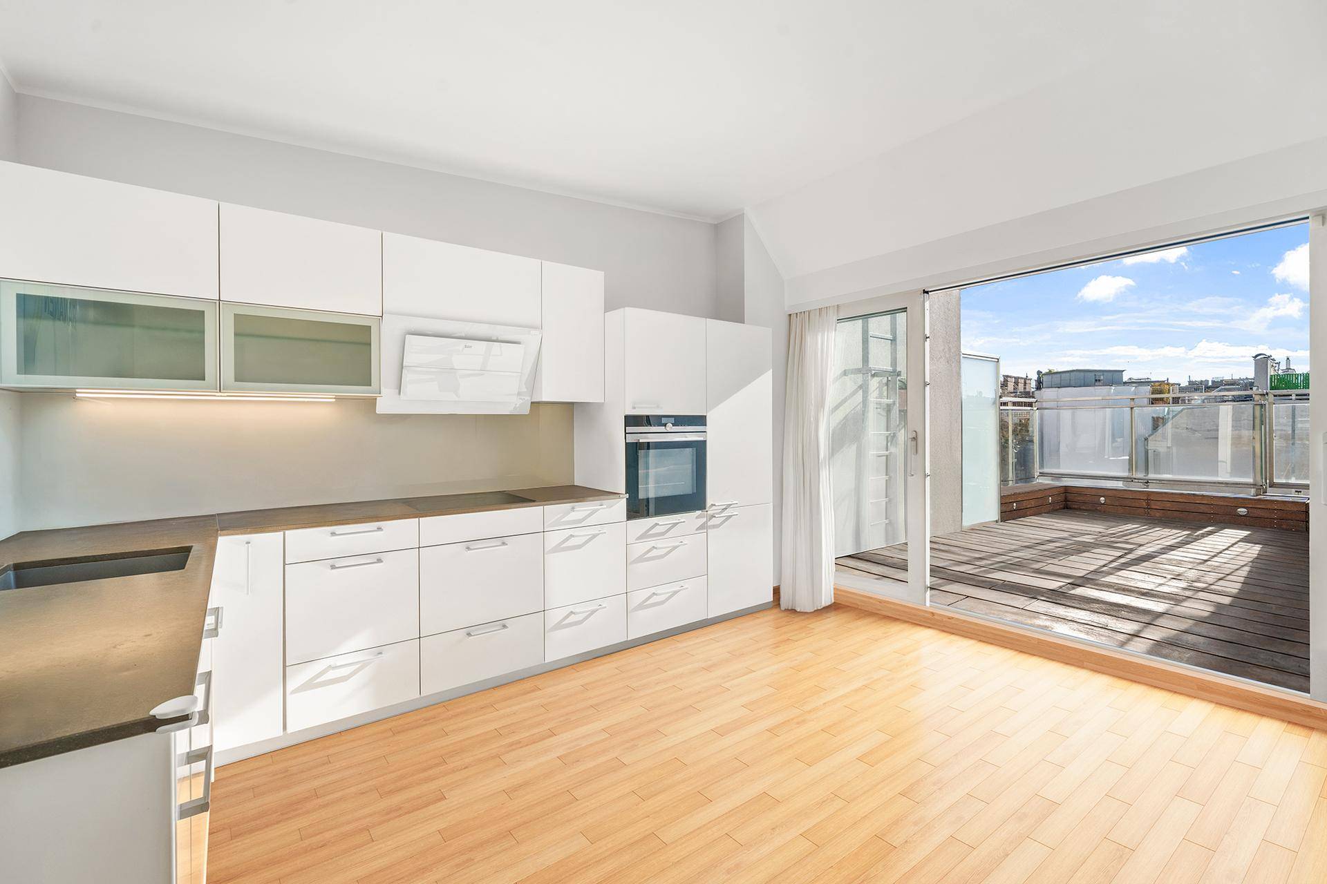 Moderne Einbauküche mit weißen Schränken und direktem Zugang zu einer sonnigen Dachterrasse.